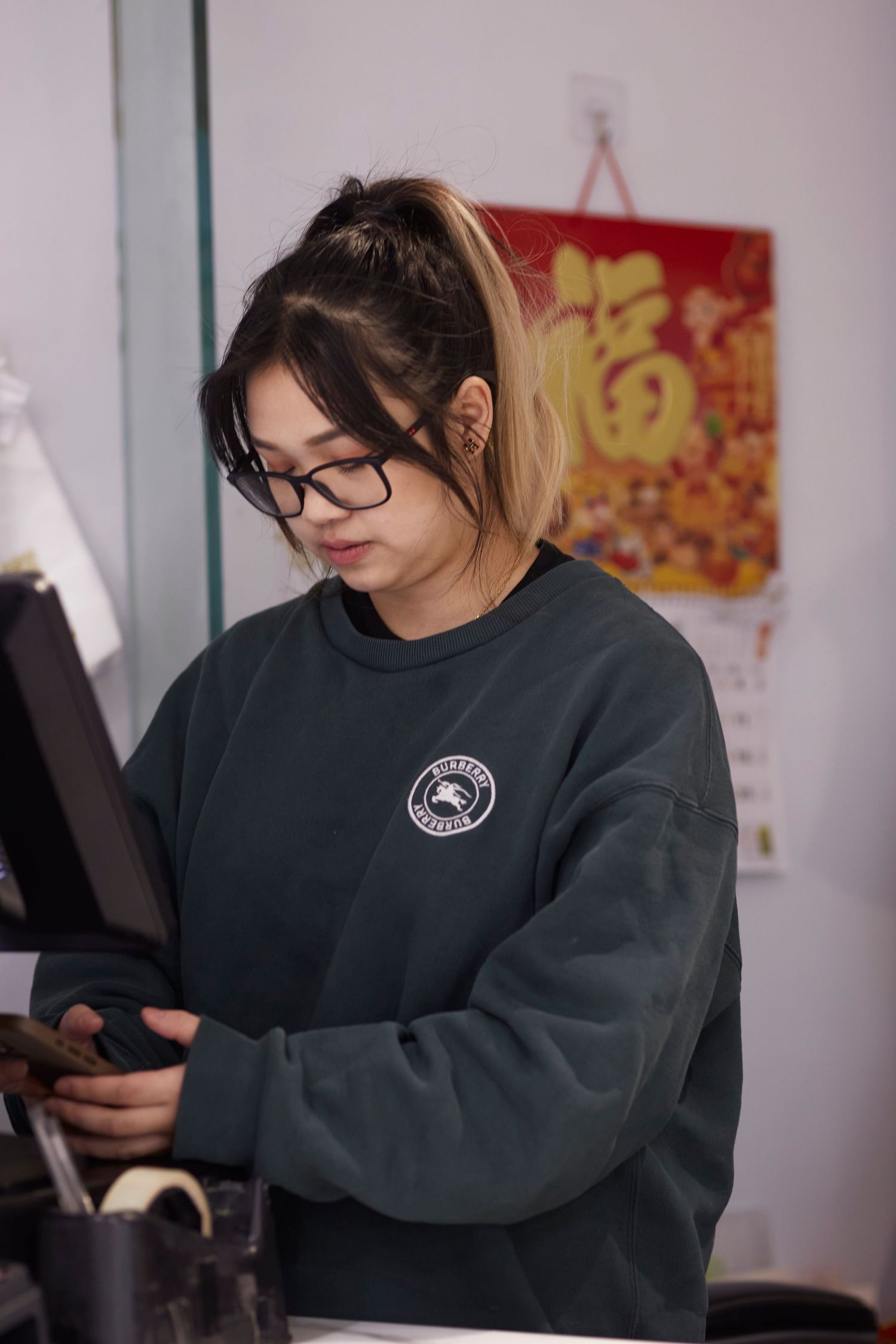 Person in dark sweatshirt working at counter with Chinese New Year decorations in background.