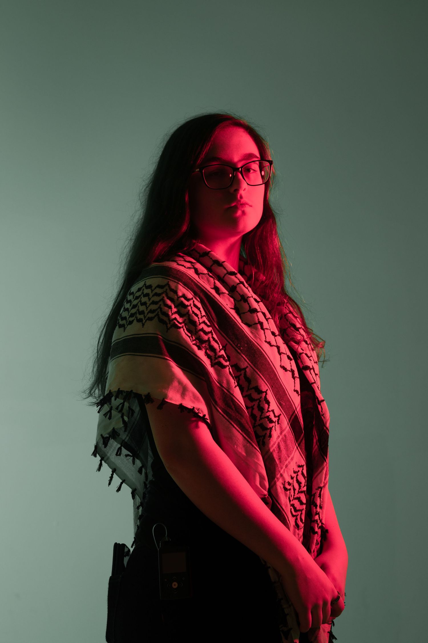 A dramatic portrait in red lighting showing someone wearing a patterned scarf and glasses.