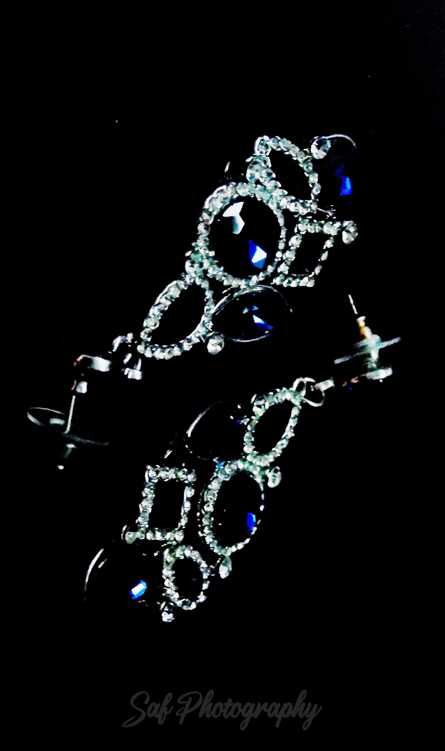 Elegant crystal hair accessories with blue accents sparkle against a black background in a flowing design pattern.