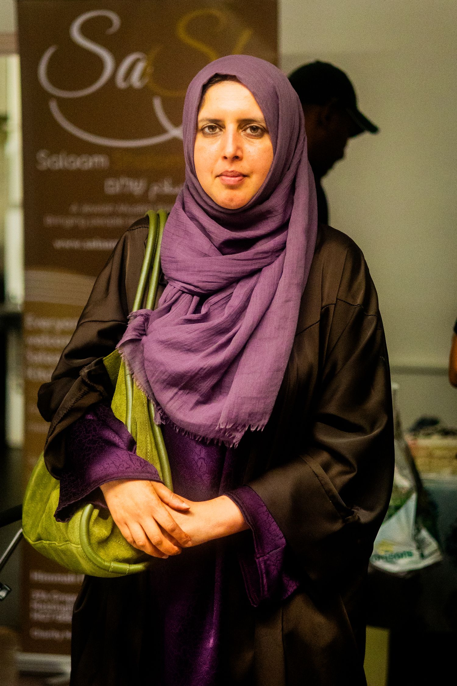 Someone wearing a purple headscarf and dark clothing sits at what appears to be a gathering.