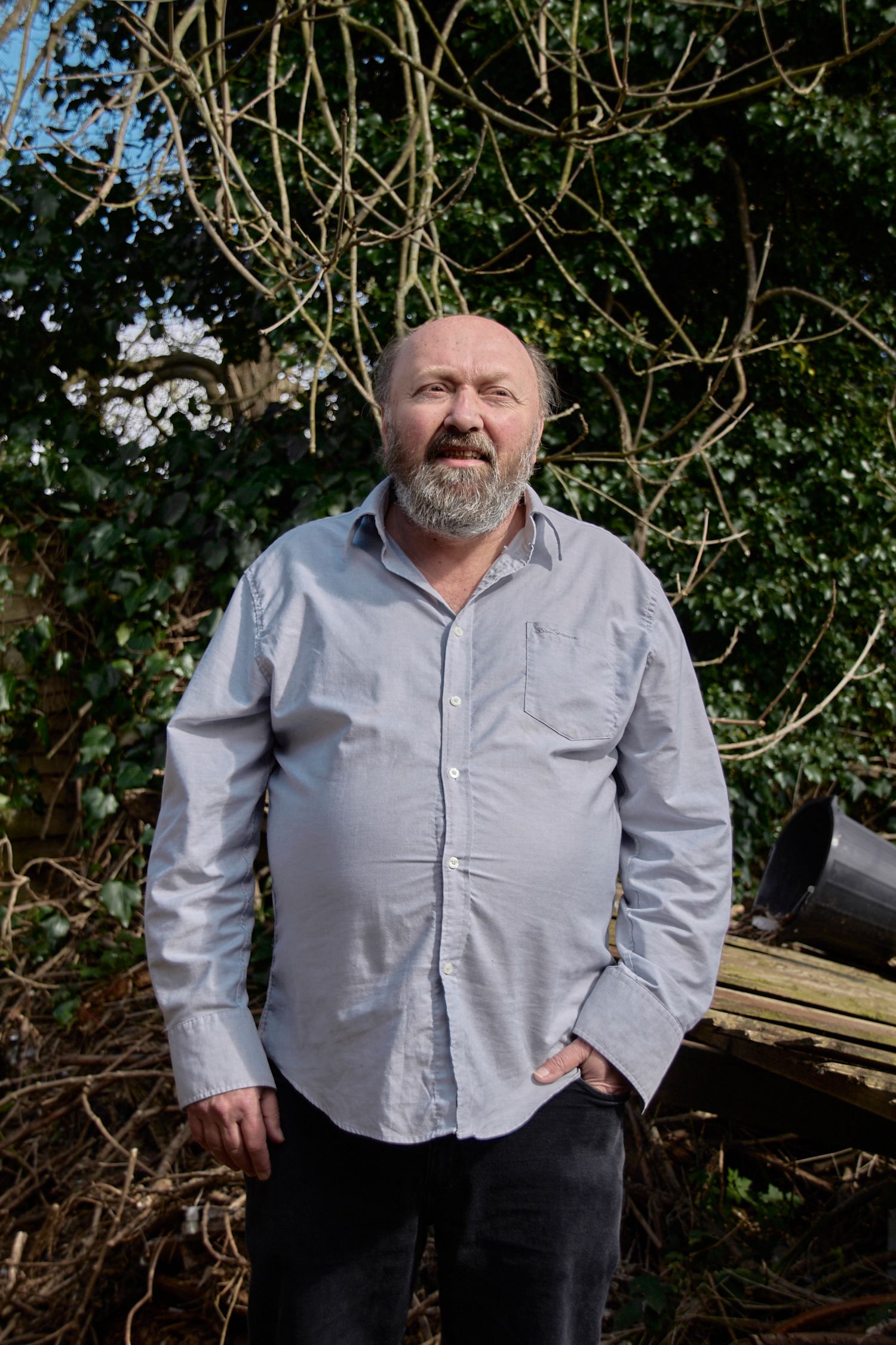 Person posed against natural backdrop with bare branches and greenery.