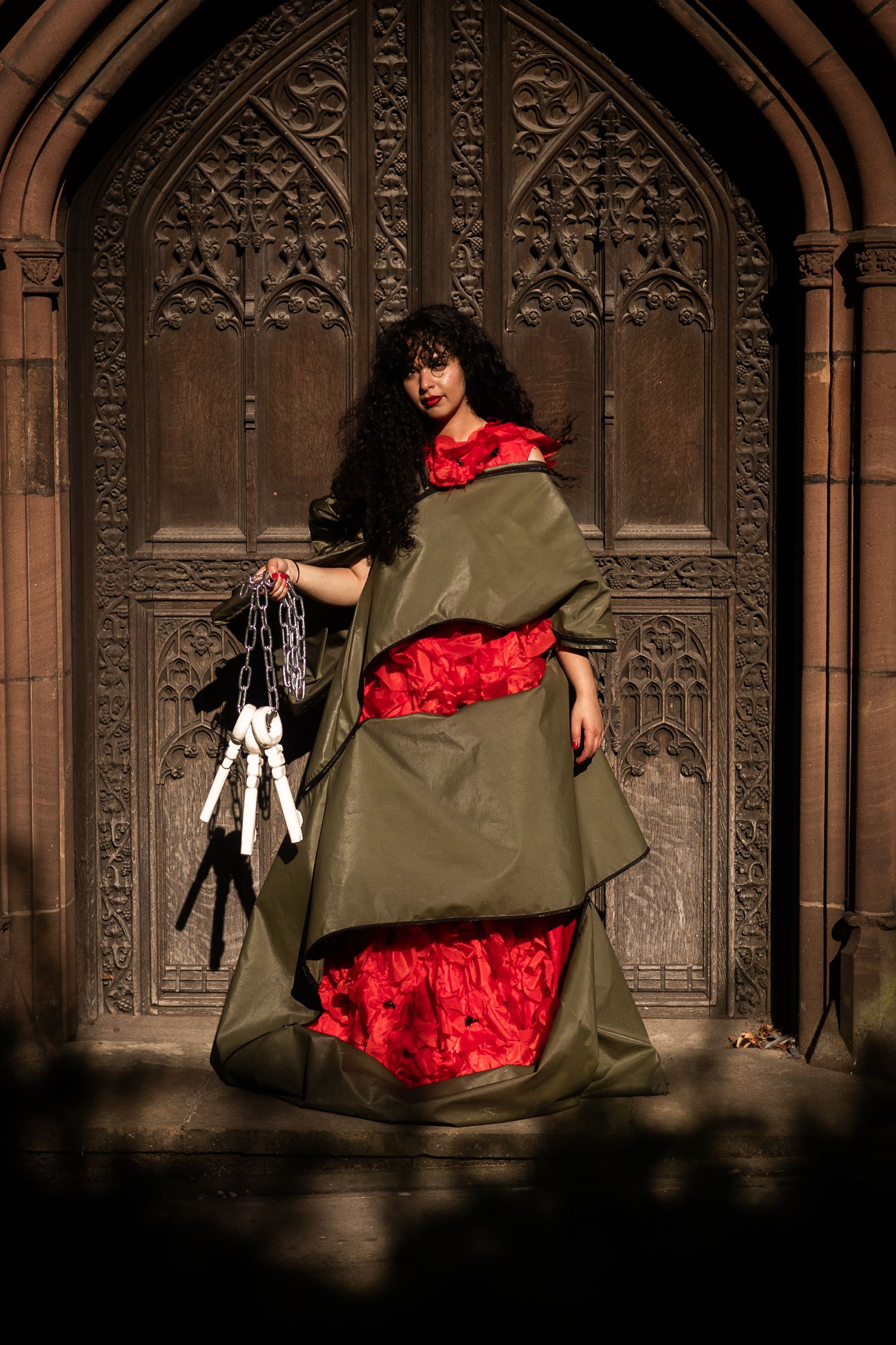 A figure in an olive green dress and red petticoat twirls dramatically against an ornate Gothic church backdrop.