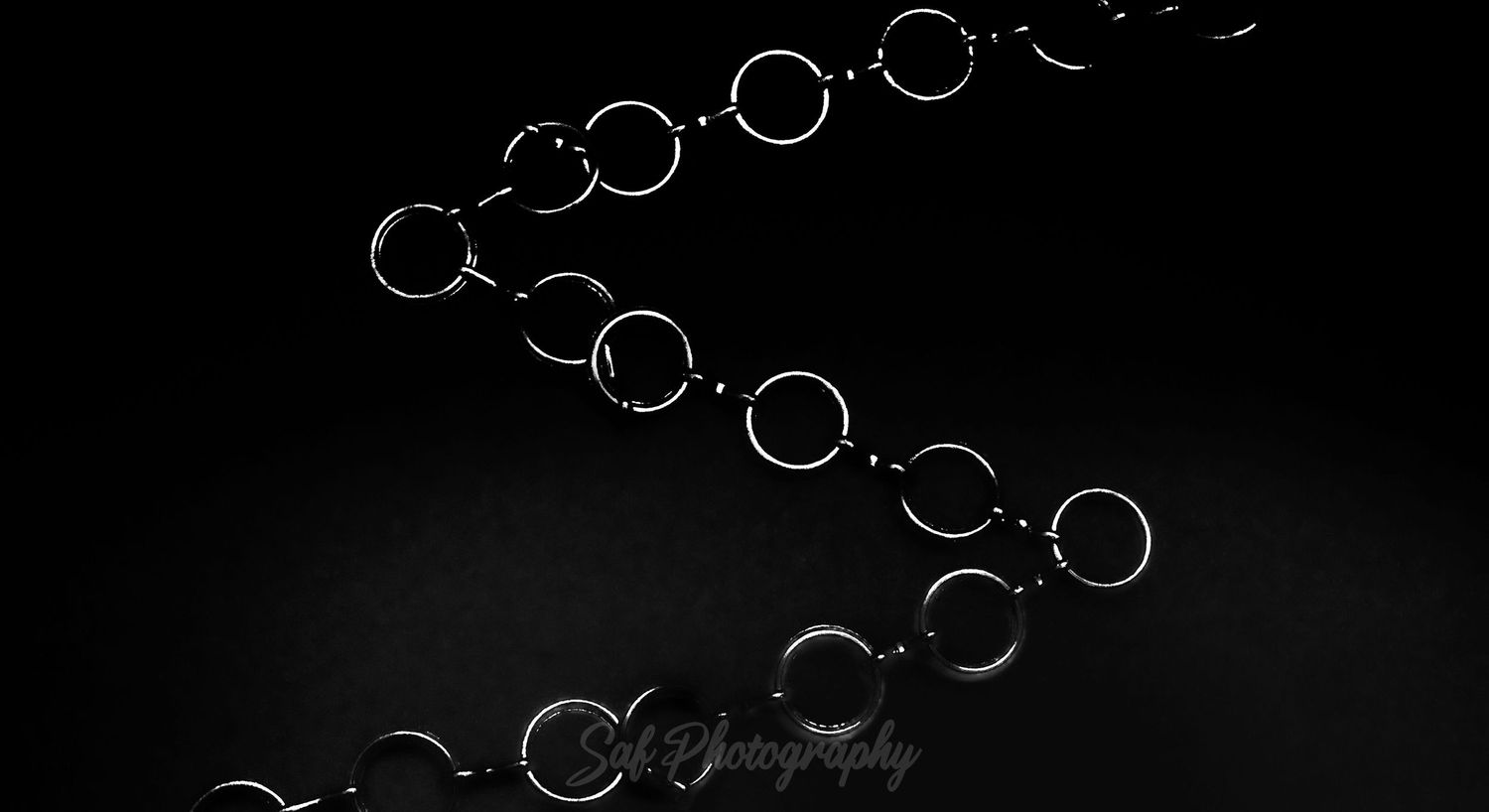 A sleek black chain bracelet with circular links arranged in a curved S-shape against a dark background.