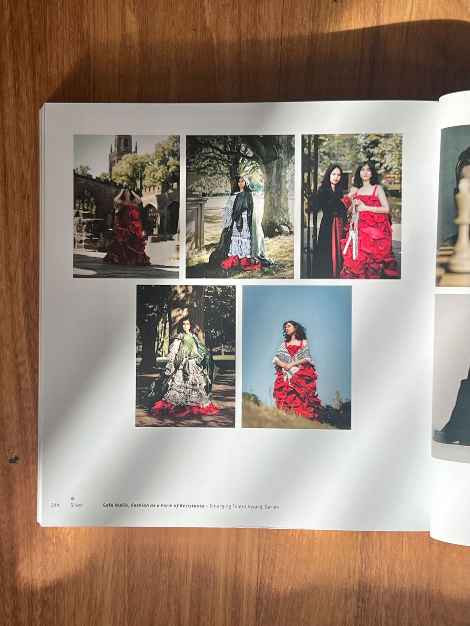 Photo book pages displayed on wooden surface showing artistic fashion photographs with red dresses and outdoor settings.
