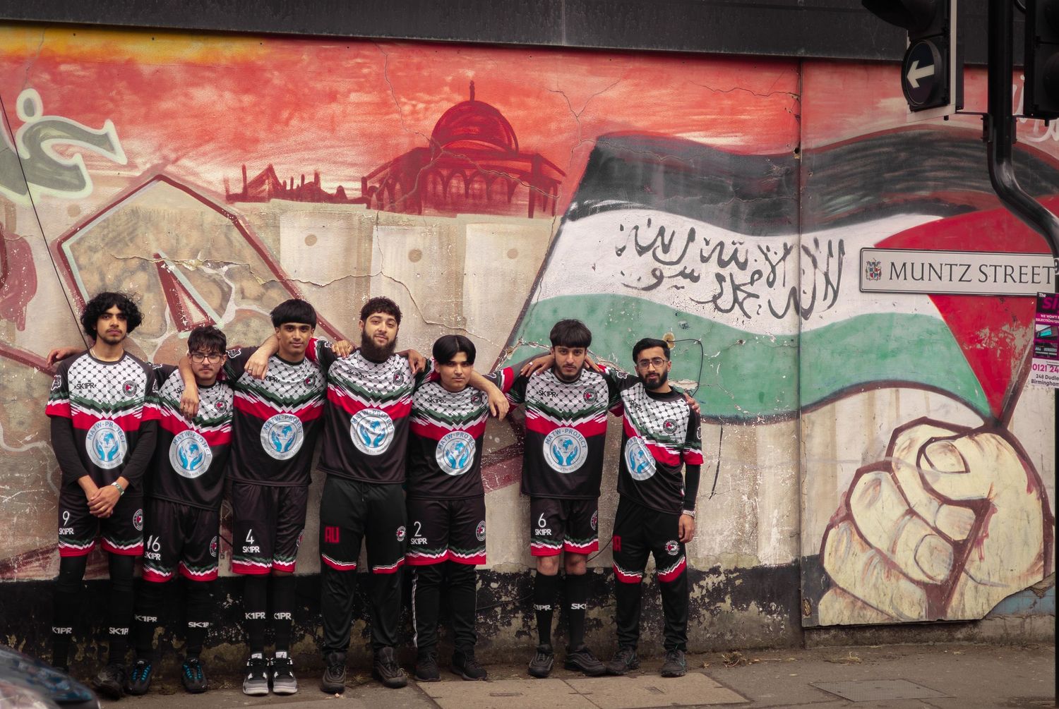 Group photo against a painted wall with Arabic text and Palestinian flag colors.