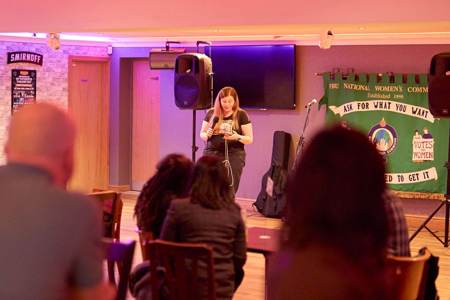 People dance and enjoy a dimly lit party space with pink and purple lighting decorating the room.