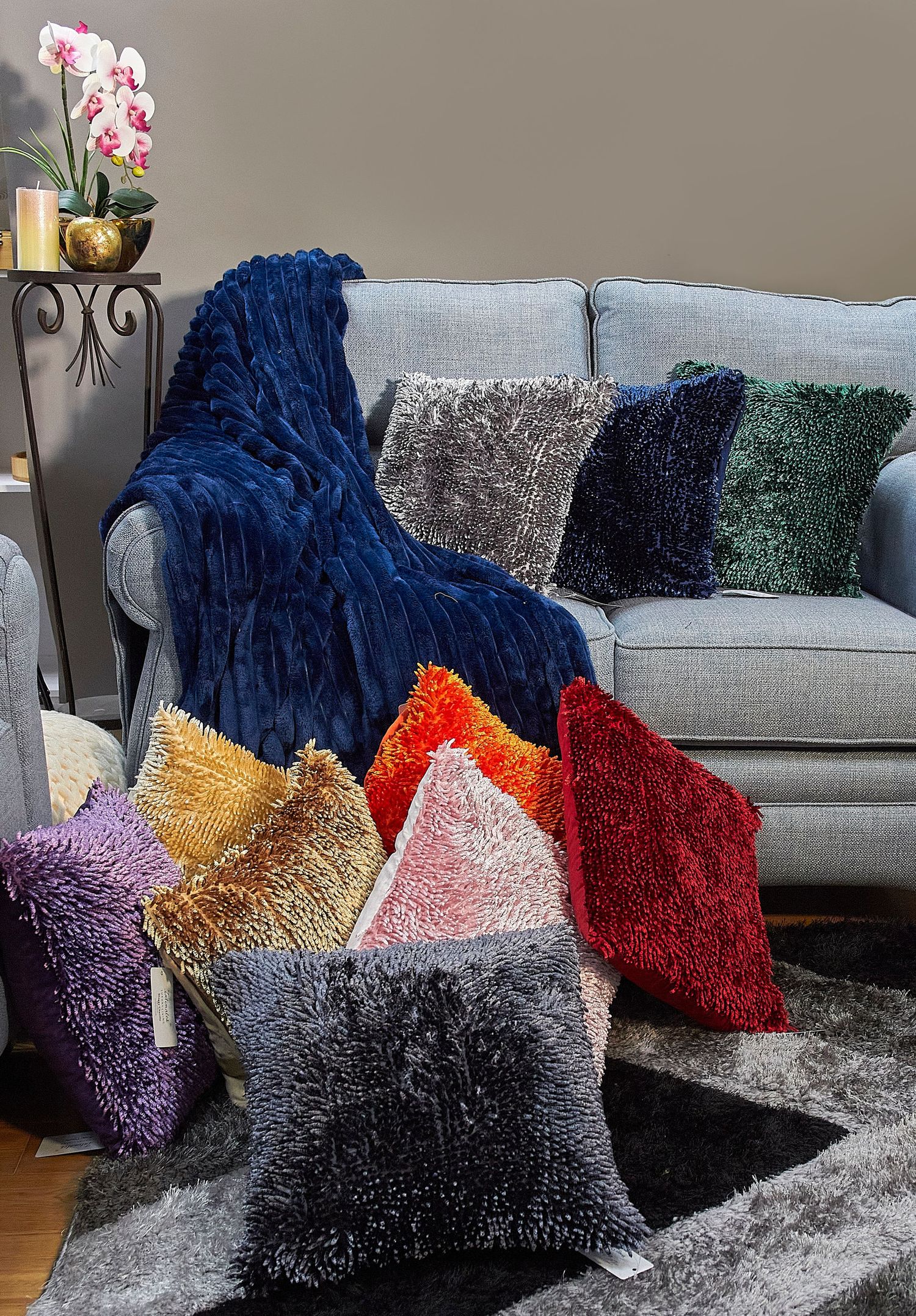 Assorted shaggy decorative throw pillows in blue, purple, red, gold and gray colors arranged on a light gray couch.