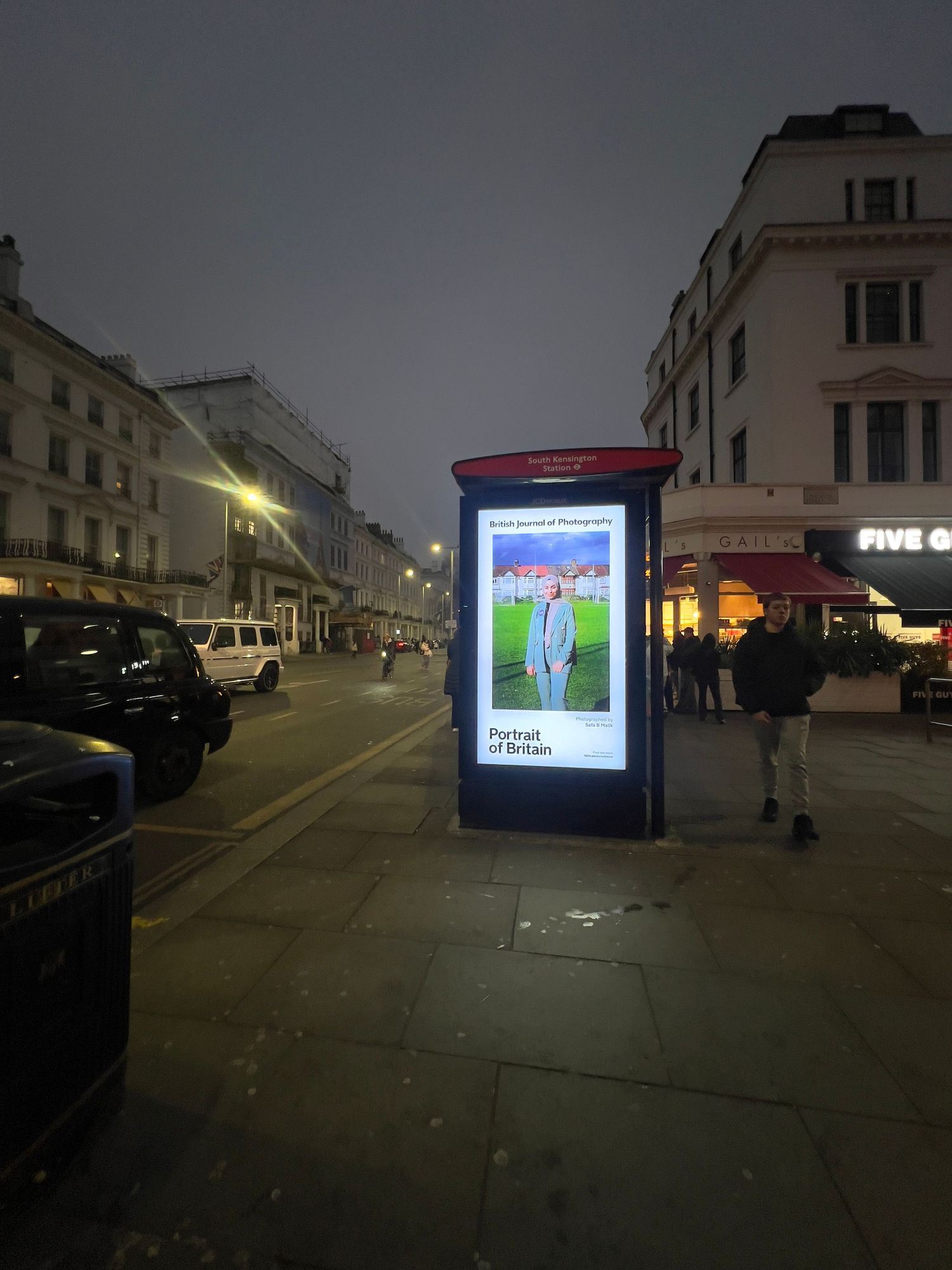 Illuminated advertising displays at night showing photography exhibition on urban street.