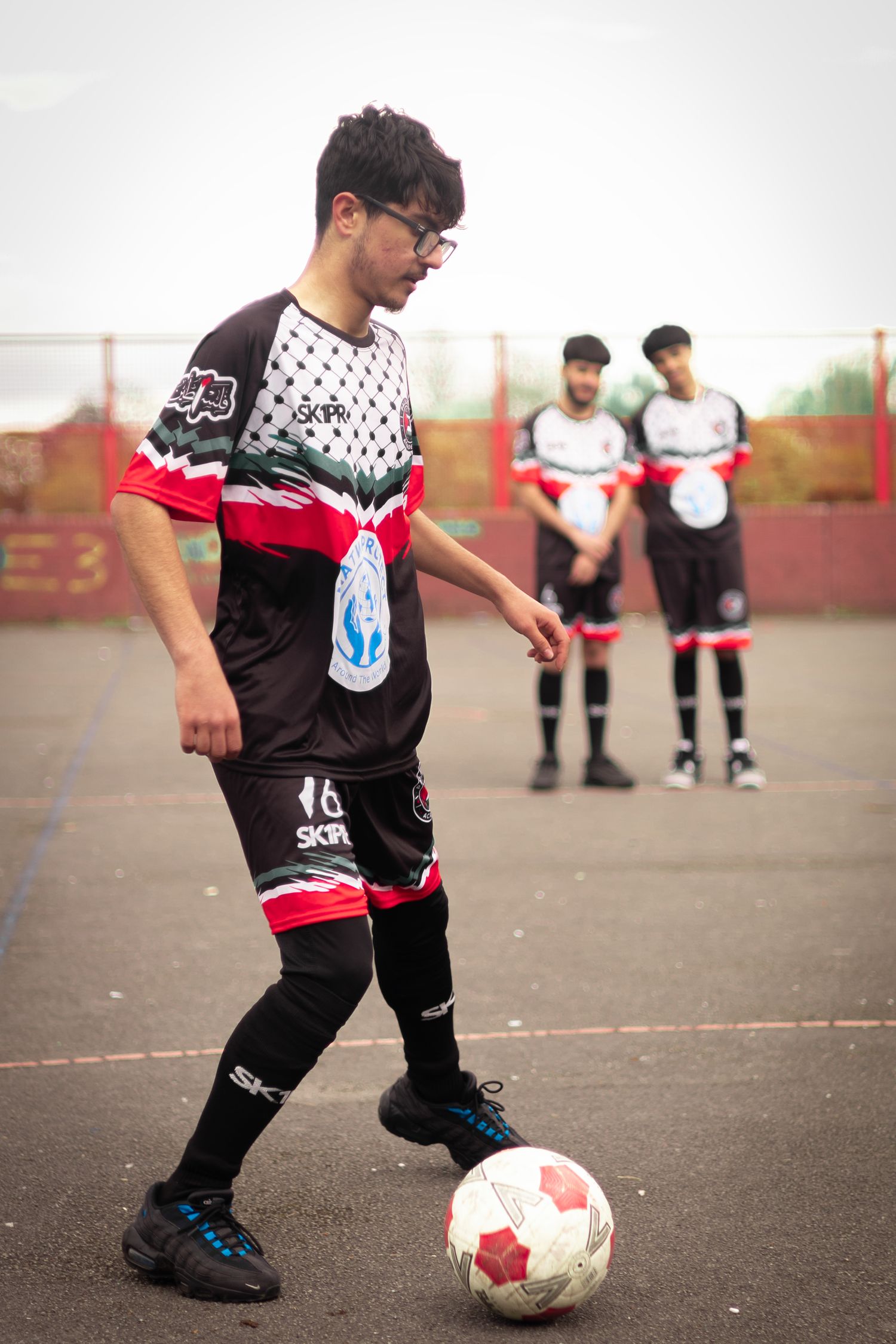 Player dribbling soccer ball wearing black and white patterned jersey with red accents.