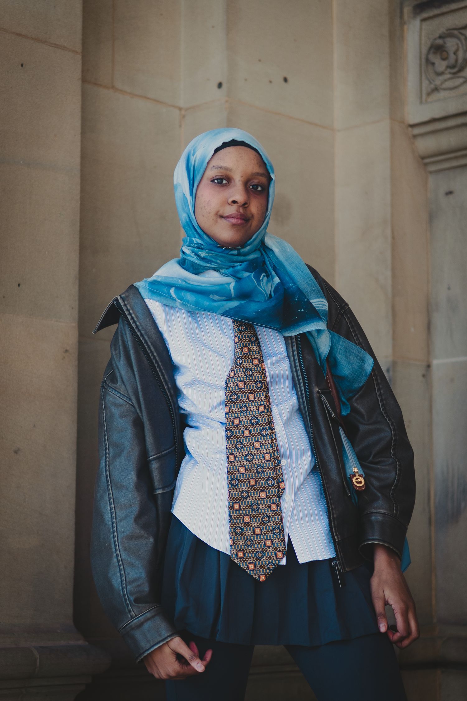 Contemporary fashion look against stone columns featuring leather jacket and patterned tie.