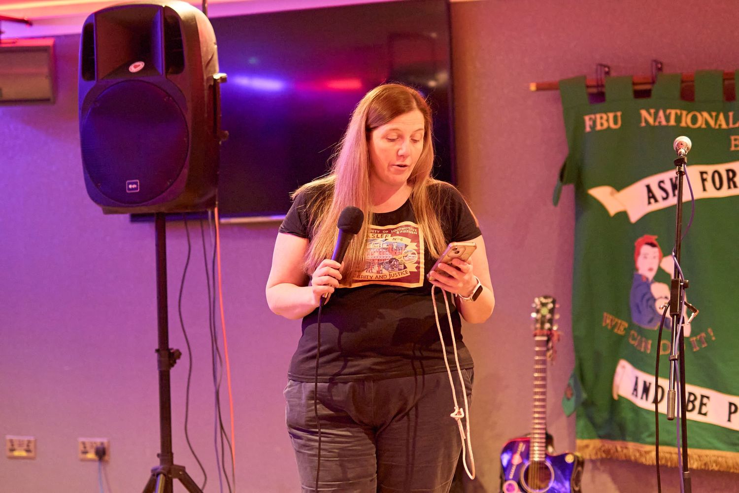 Karaoke performance setup with colorful stage lighting and speakers against a green backdrop and LCD display screen.
