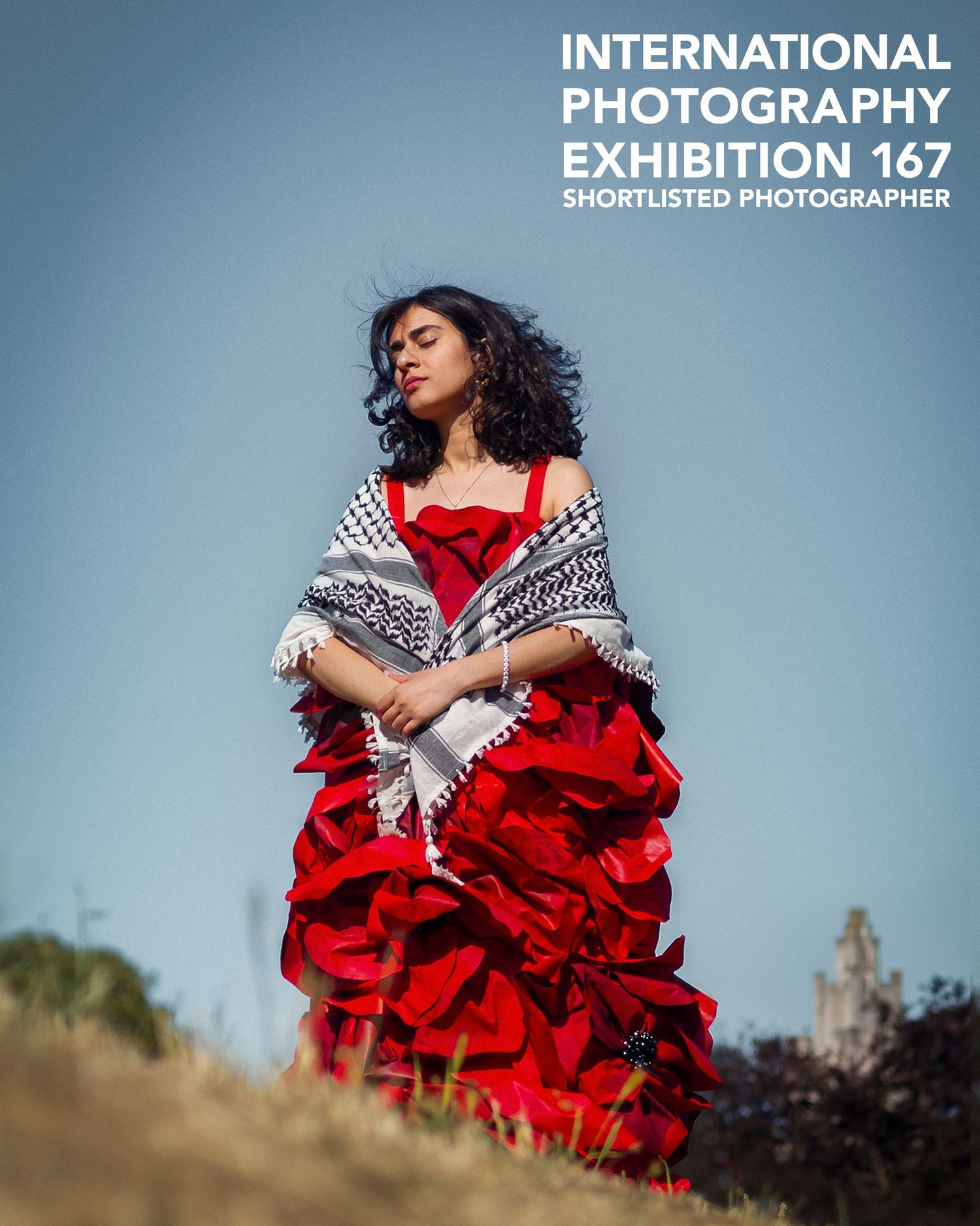 Woman in red ruffled gown with keffiyeh shawl poses outdoors at International Photography Exhibition 167.