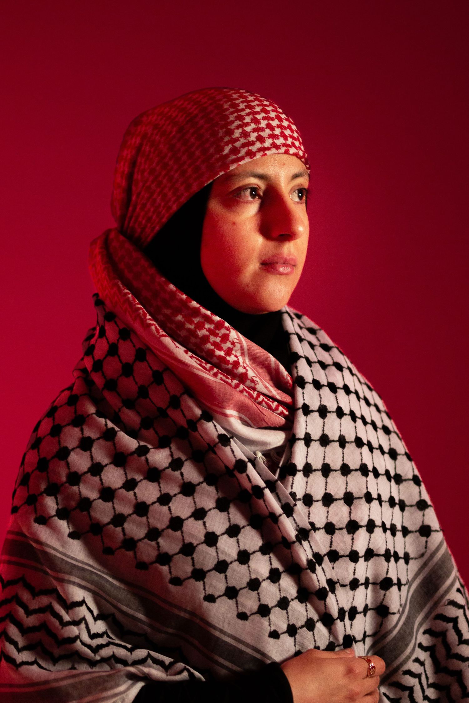 Woman wearing traditional red and white keffiyeh scarf and hijab, posed against a deep red background.
