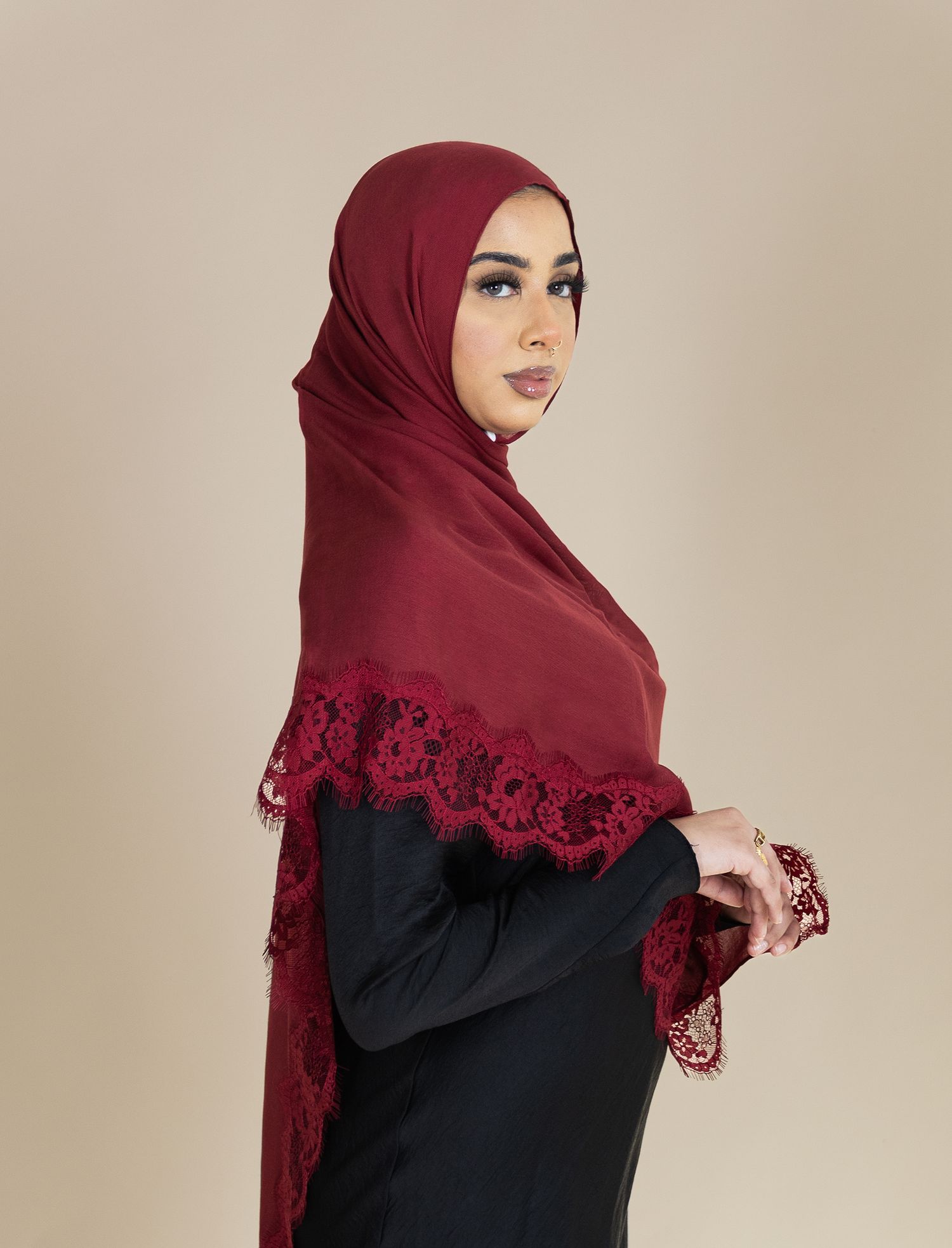 A sequence of photos showing a burgundy hijab with black lace trim worn with a black dress against a beige background.