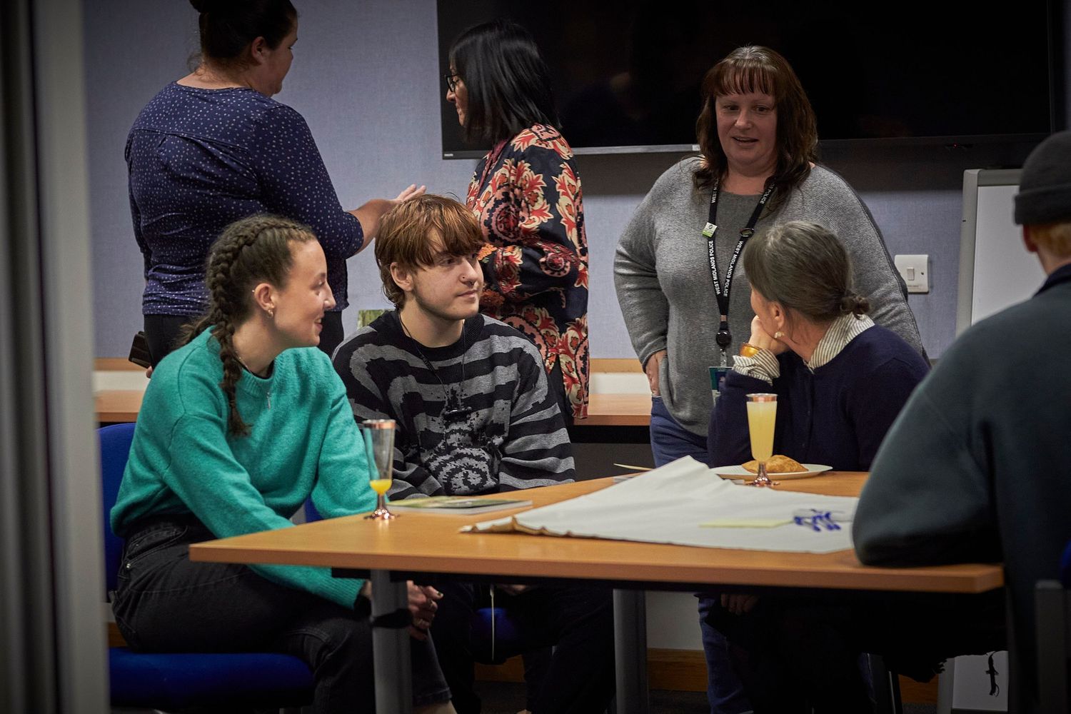 Students gather around a table during a classroom discussion as an instructor stands nearby.
