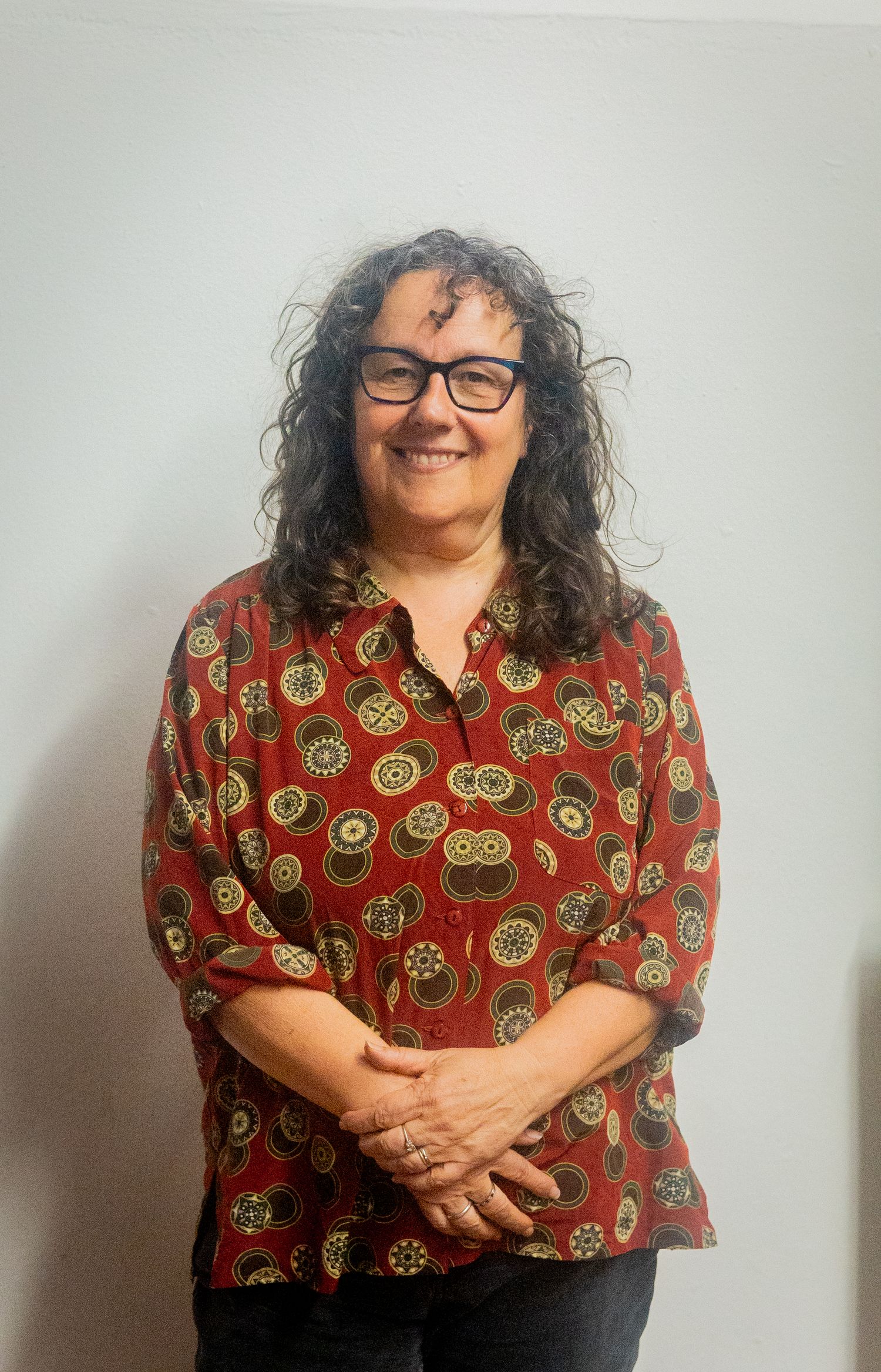 Person in glasses and red patterned top posing against white background.