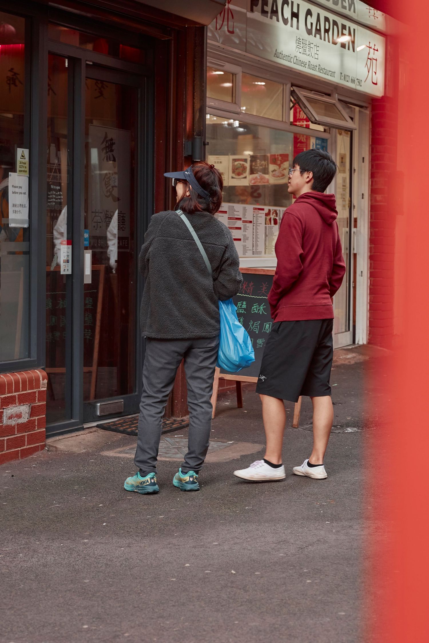 Two people standing outside a restaurant called Peach Garden.