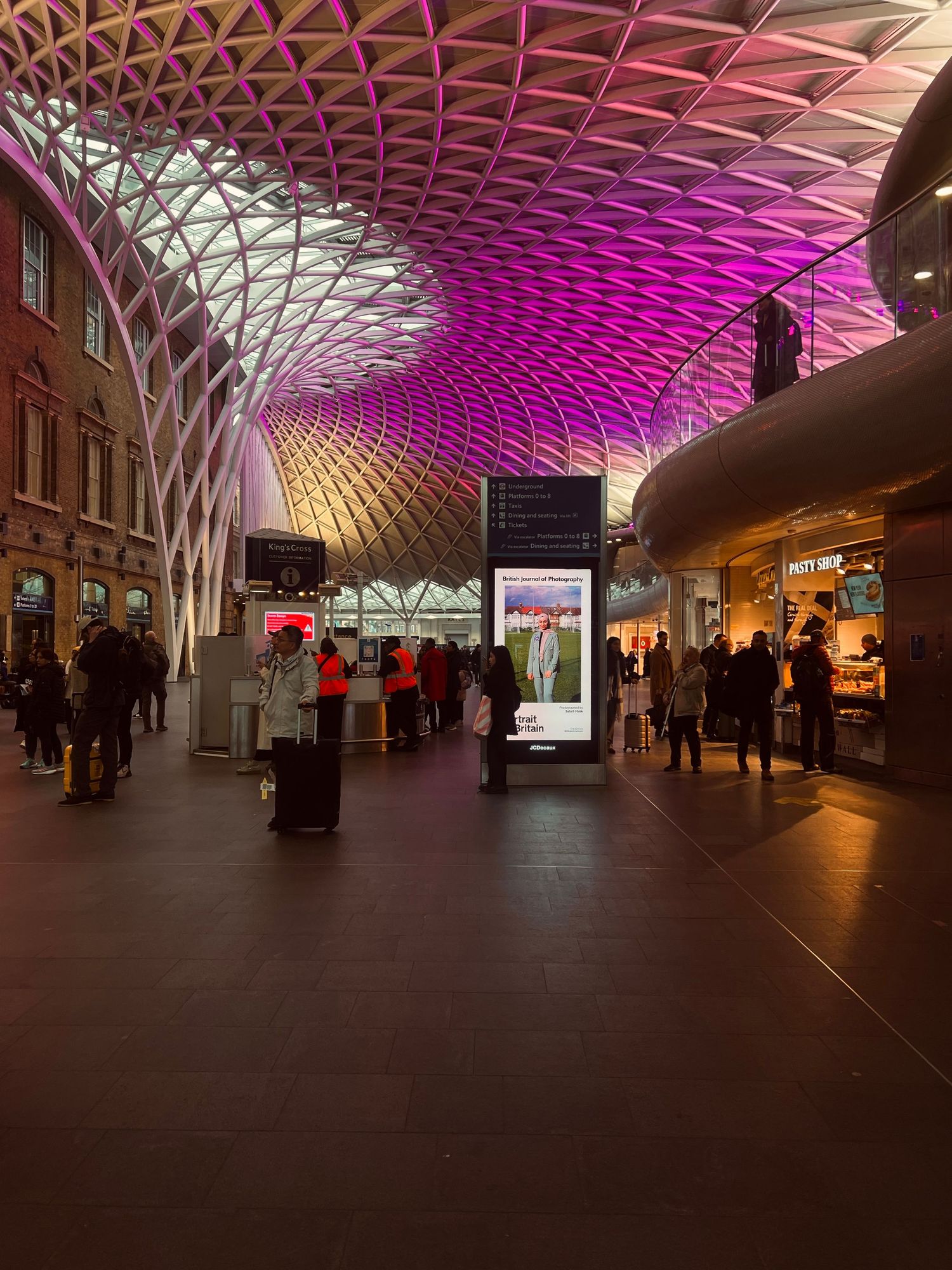 Kings Cross station concourse with pink illuminated ceiling and digital displays.