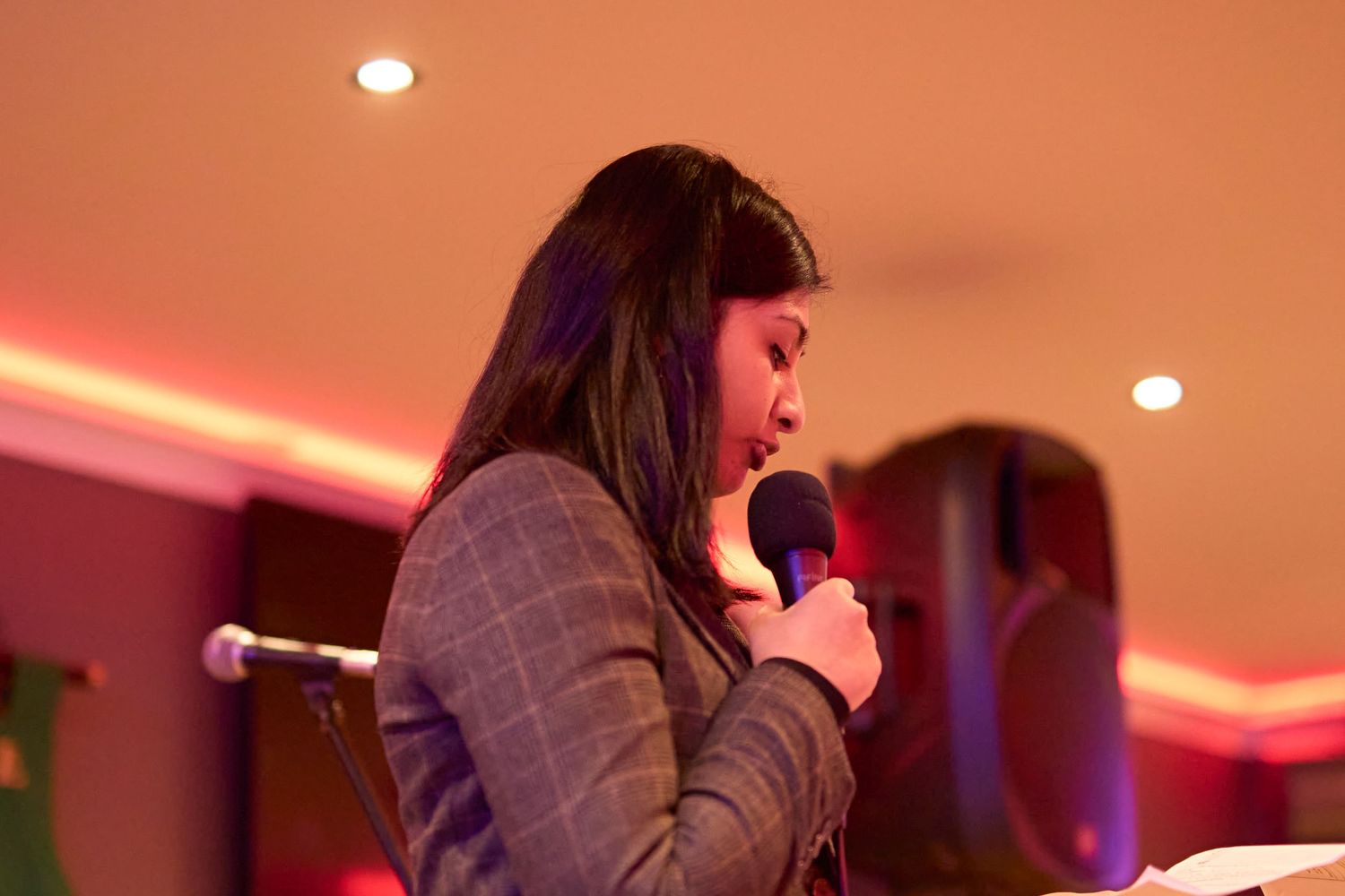 People perform at a live music venue with warm red lighting and atmospheric ambiance in the background.