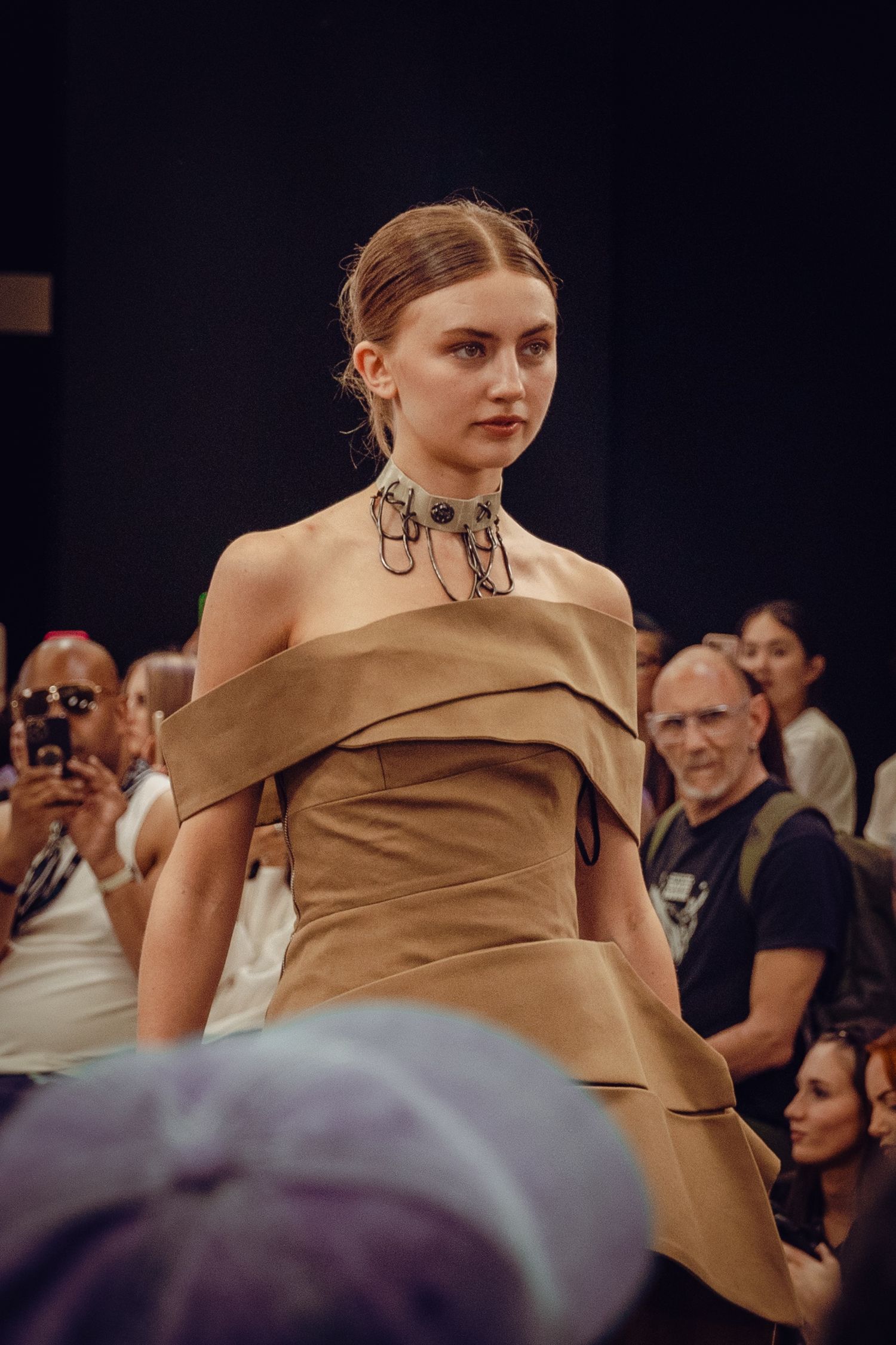 Elegant caramel-colored off-shoulder dress displayed at high-end fashion runway show.
