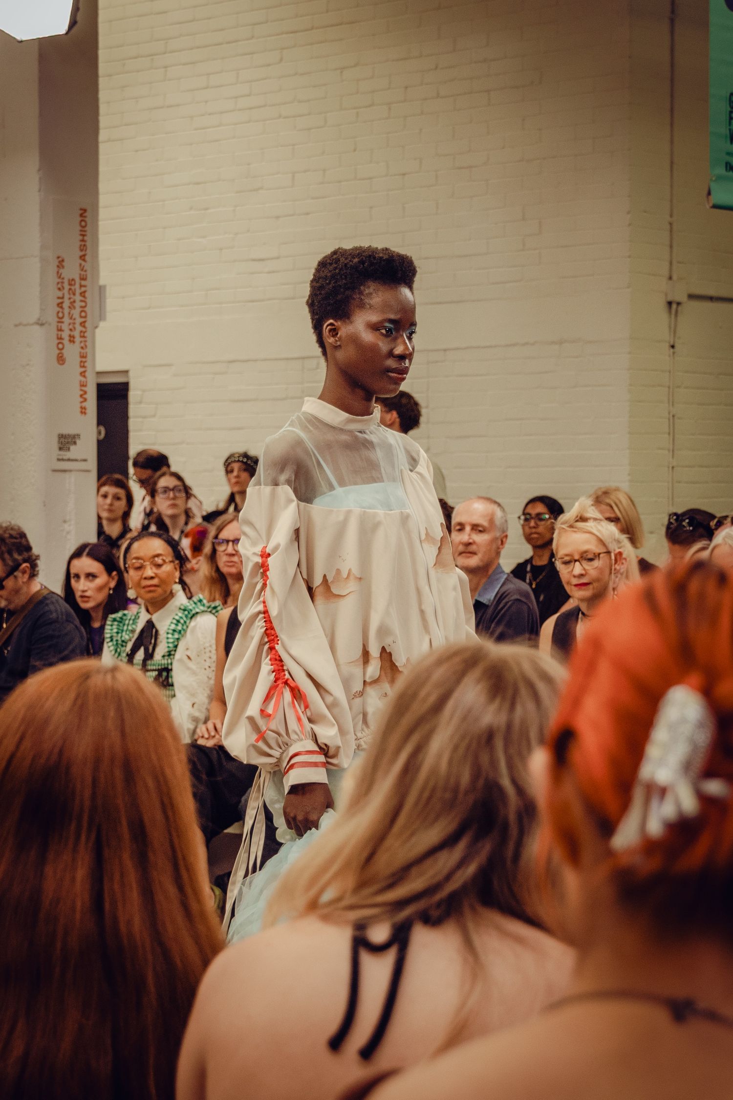 Model showcasing sheer white avant-garde dress design on fashion runway.