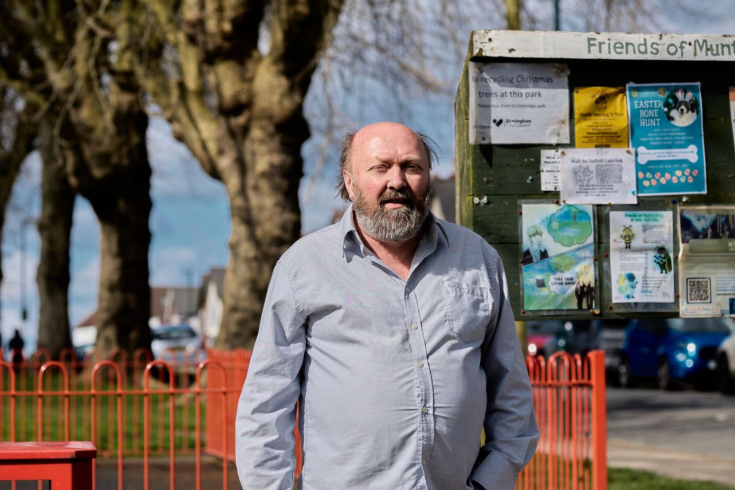 Person in light colored shirt posing outdoors near information boards and orange fencing.