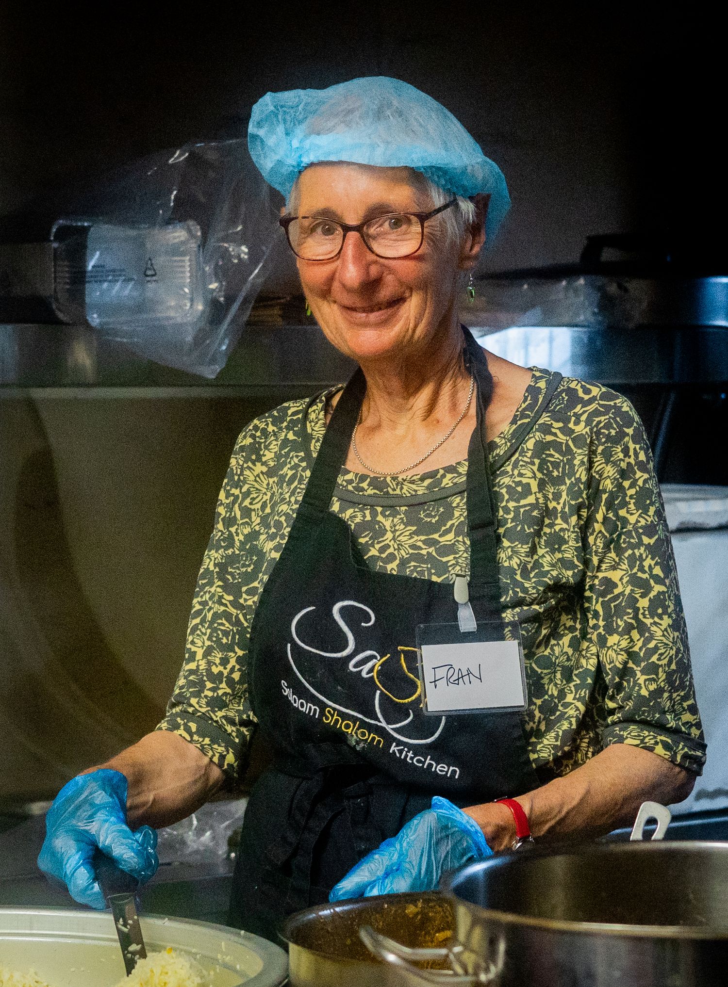A person wearing a hairnet and apron serves food in a commercial kitchen setting.