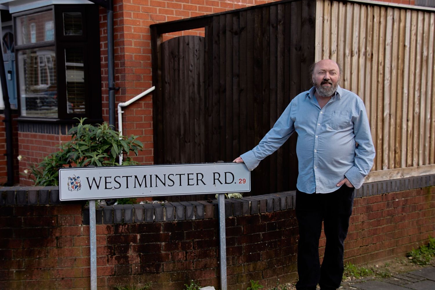 Person standing next to Westminster Road street sign by a wooden fence.