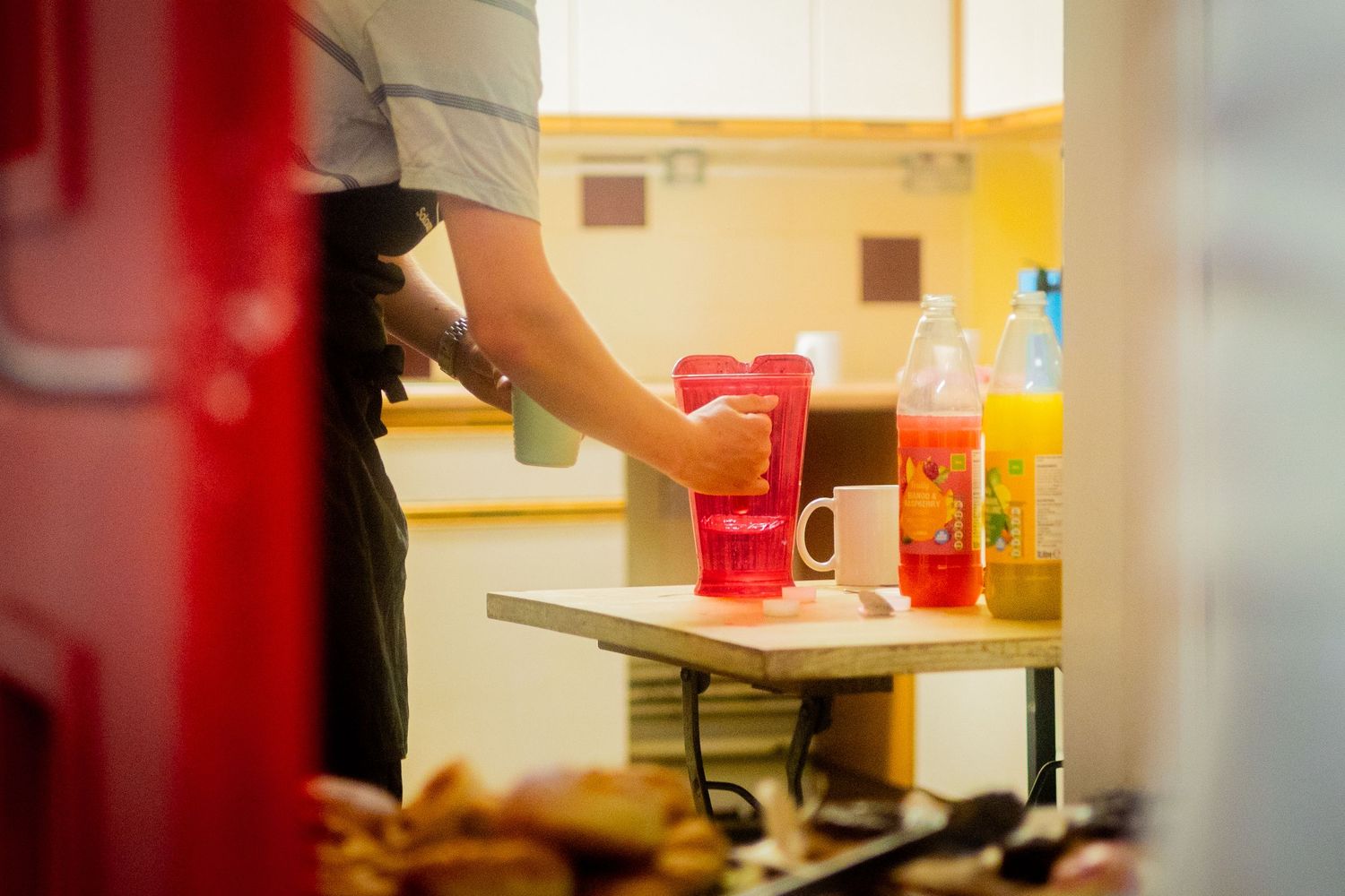 Workers prepare food on stainless steel tables in a bright kitchen setting.