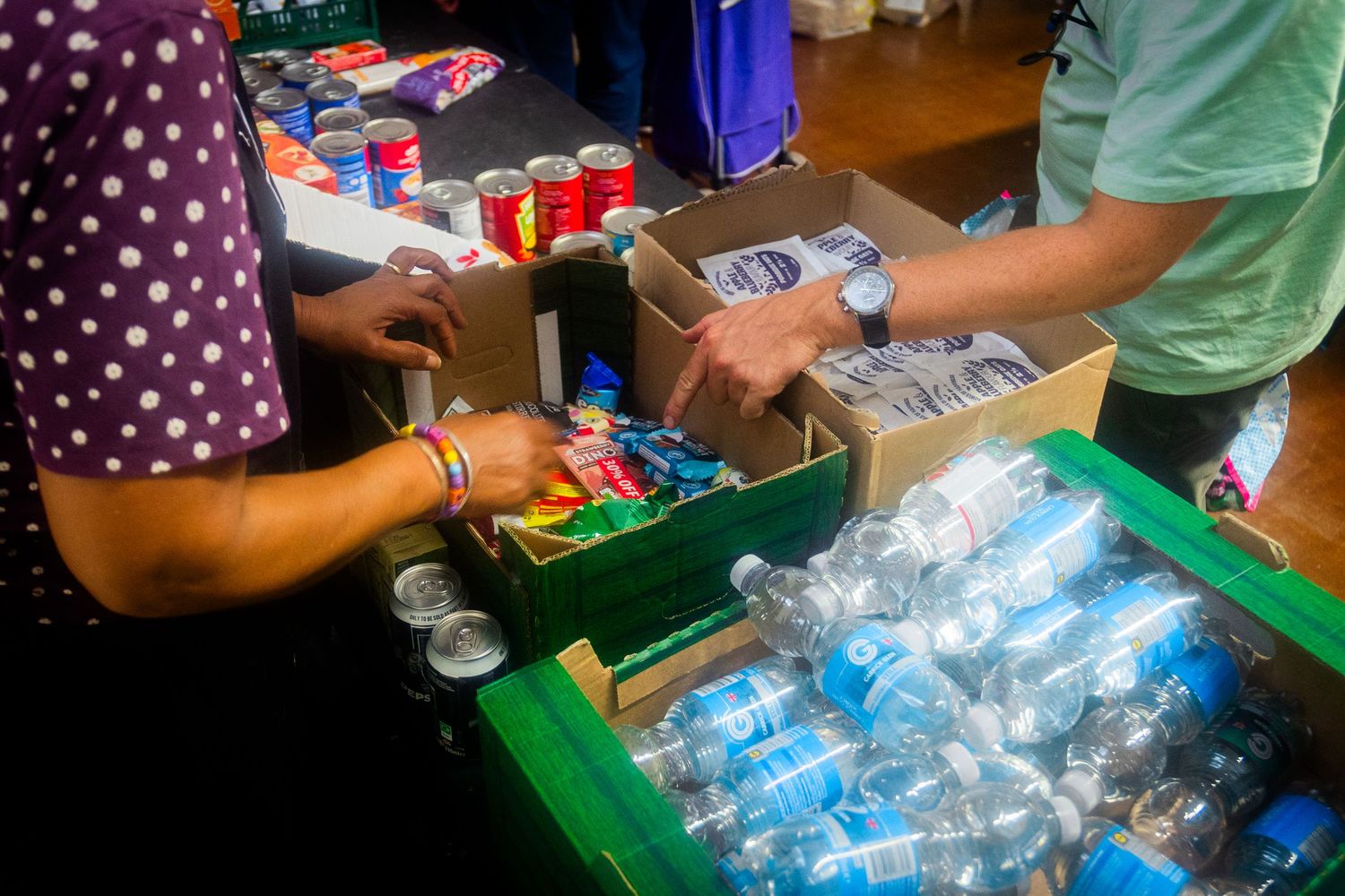 Volunteers distribute water bottles and packaged goods from organized bins.