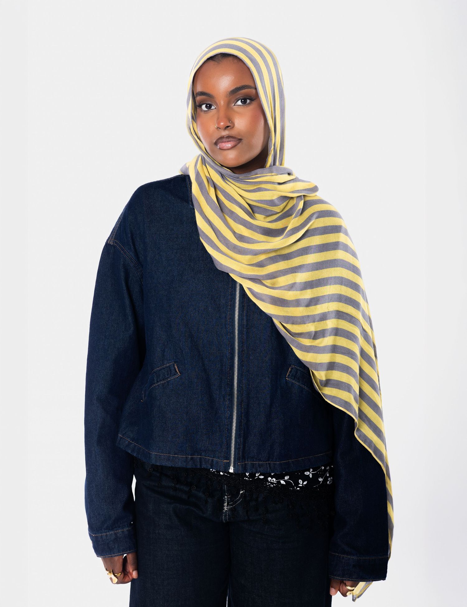 Woman wearing yellow and gray striped hijab with dark denim jacket and black sequin belt.