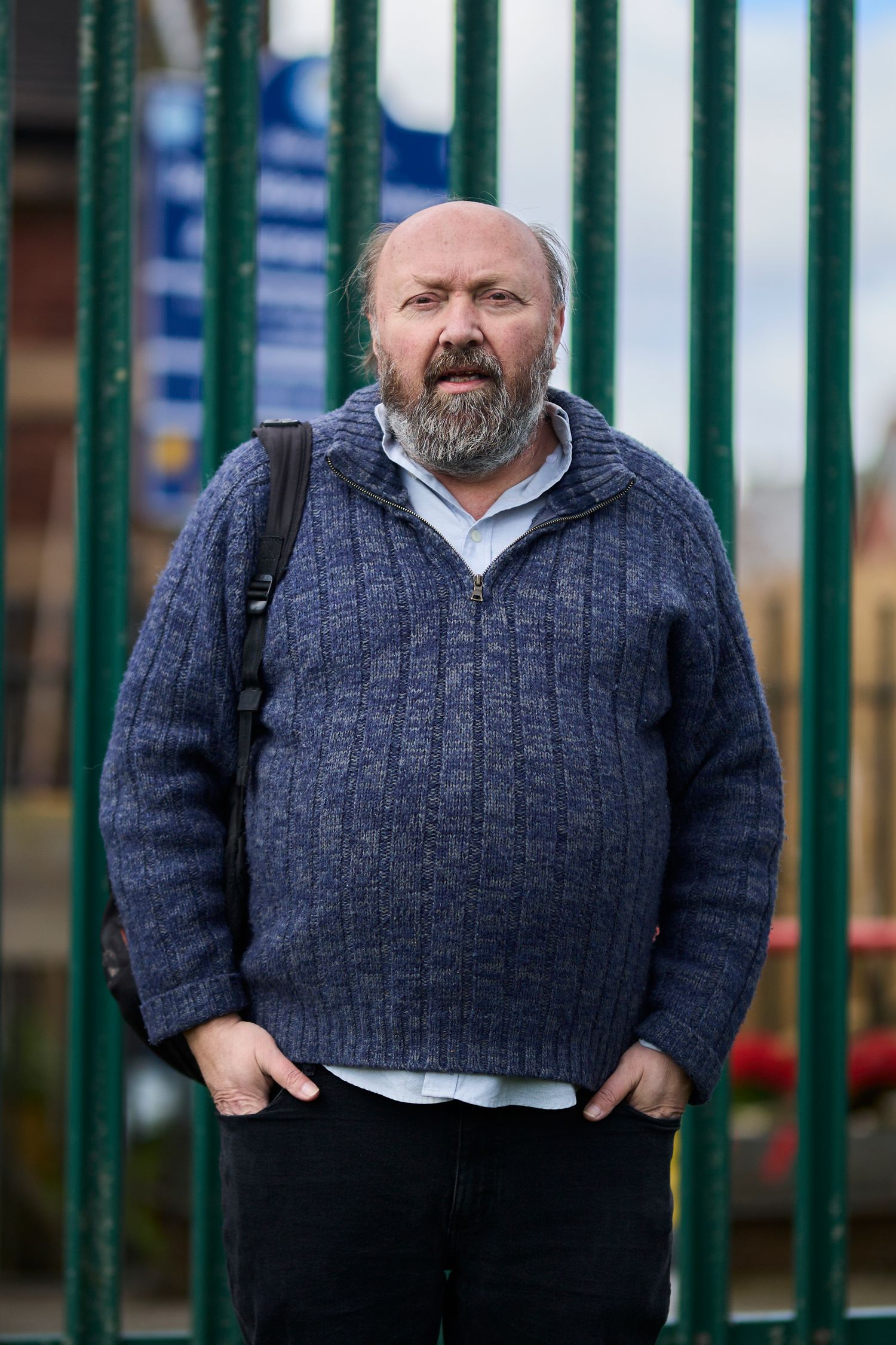 Person in navy sweater standing beside green metal fence outdoors.