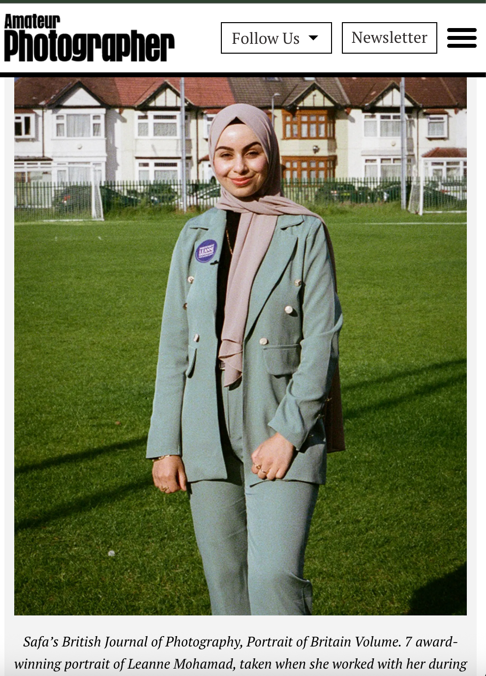 A person in a mint green suit and beige hijab poses on a lawn in front of suburban houses in a British photography portrait.