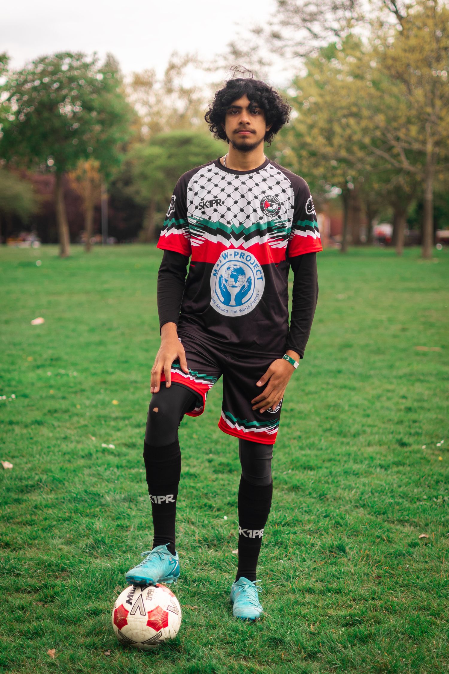 Soccer player in black and white patterned jersey poses with ball on grassy field.
