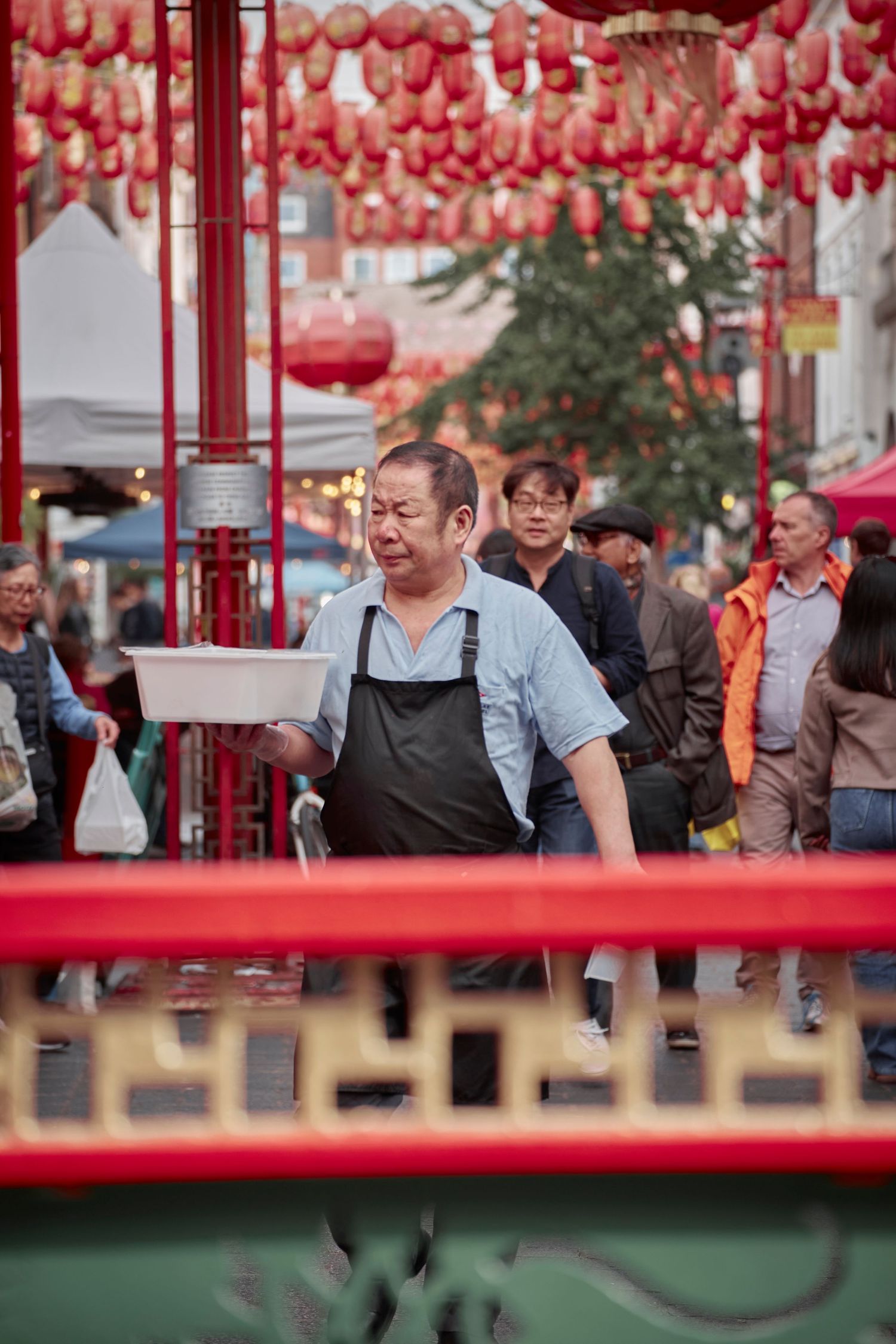 Food vendor in apron working under red lantern decorations at street festival.