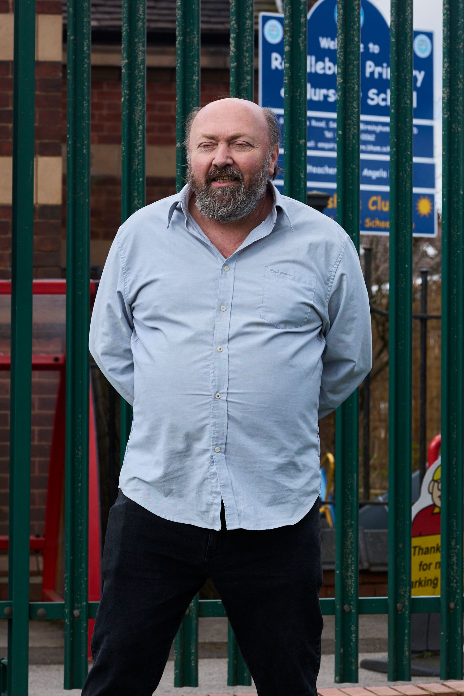 Person wearing light blue shirt stands near green metal fence.