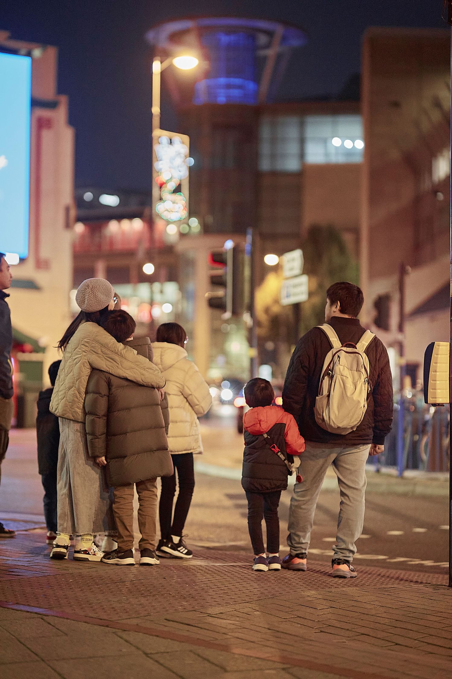 Groups of people standing outside on an urban sidewalk at night.