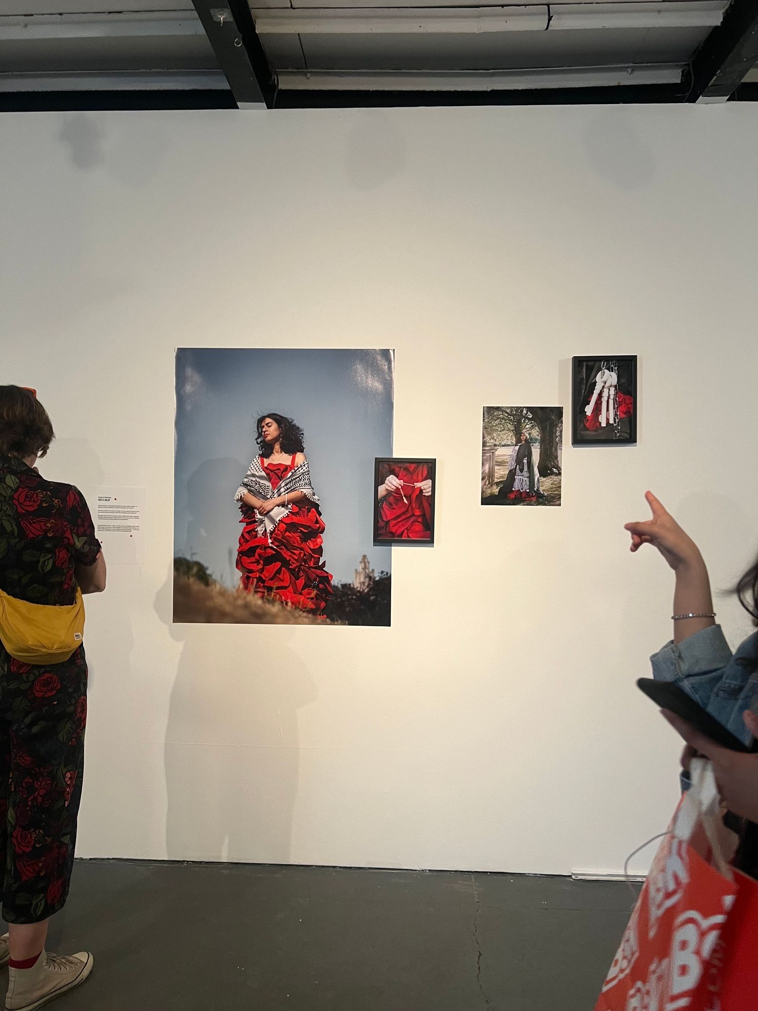 Art gallery visitors viewing photos of a woman in a red flamenco dress displayed on a white wall.