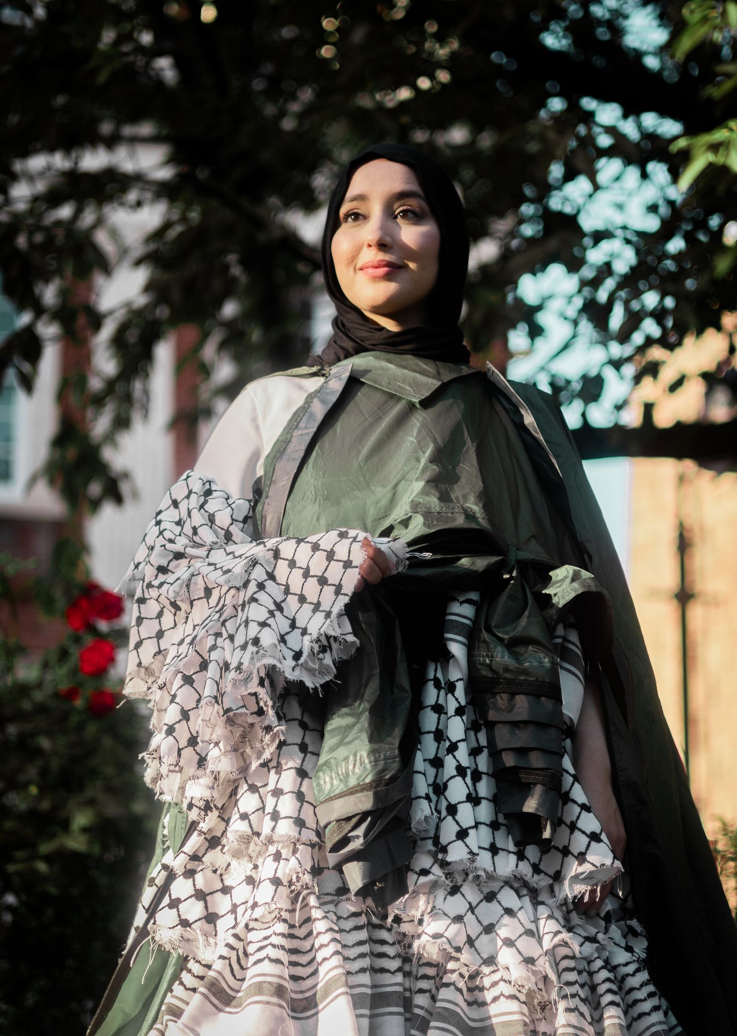 A fashion model wearing a green hijab and an elegant black and white patterned dress poses outdoors at sunset.