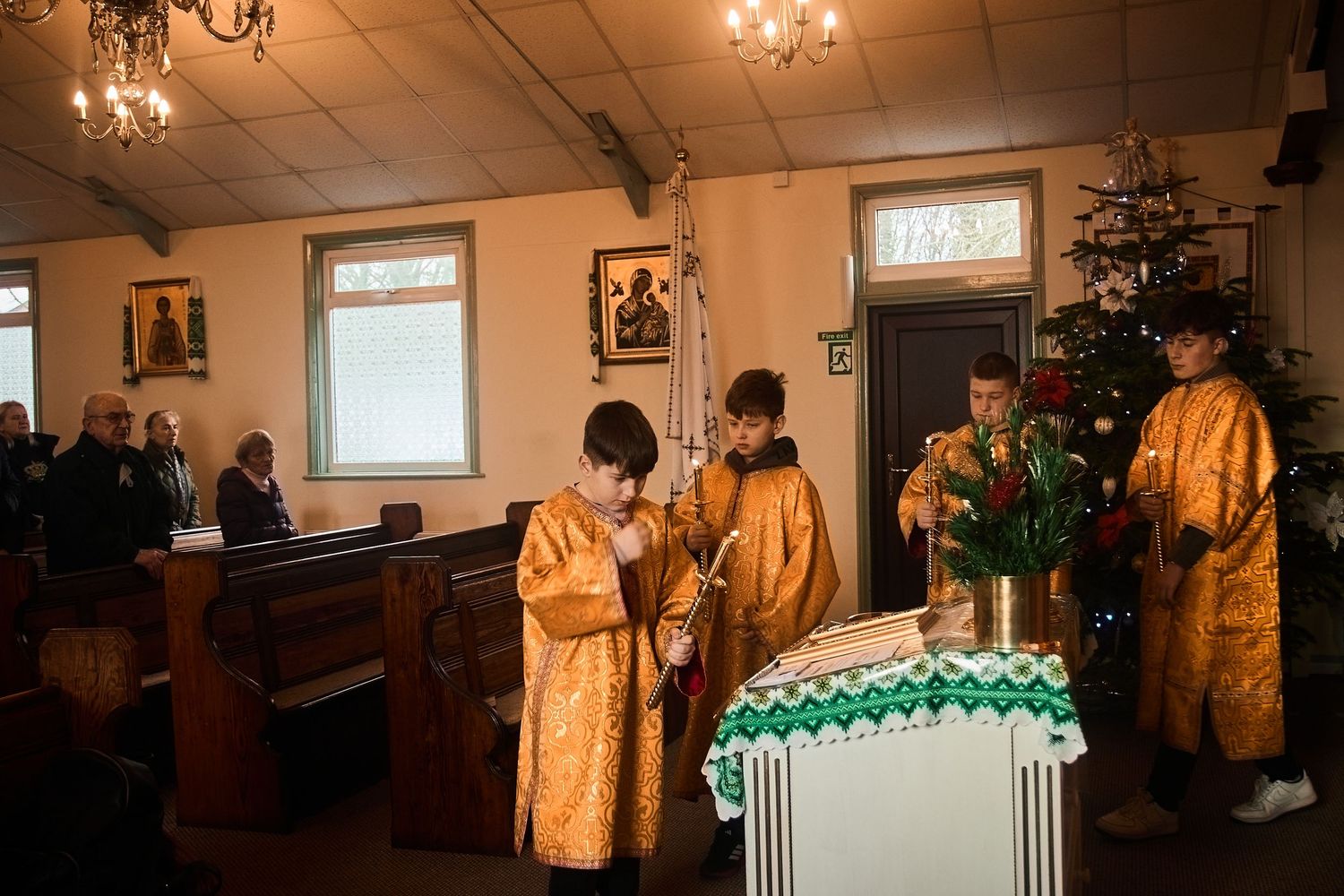 Orthodox clergy in golden vestments conducting service near decorated Christmas tree.