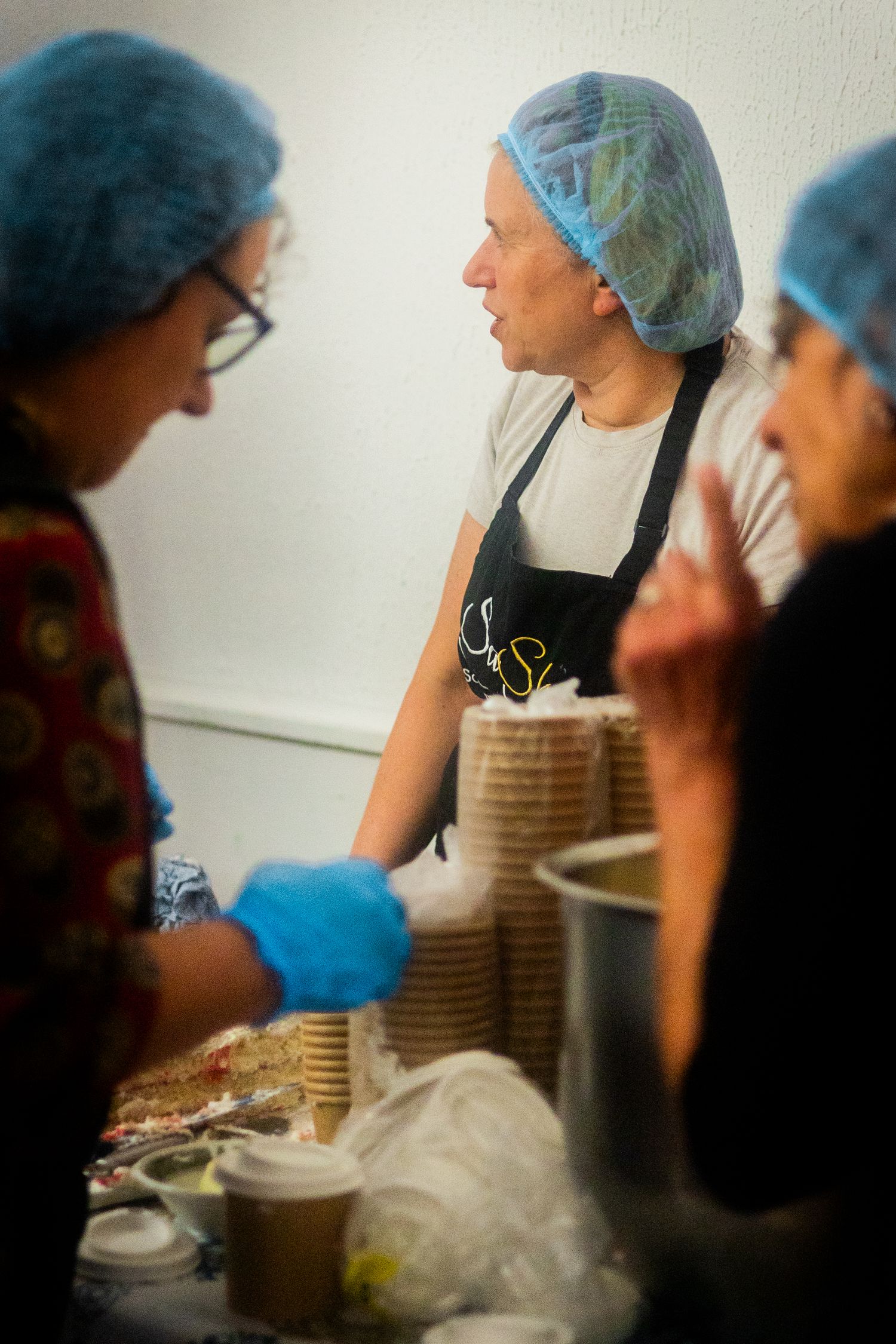 Food preparation area with workers wearing blue hair nets working at stations.