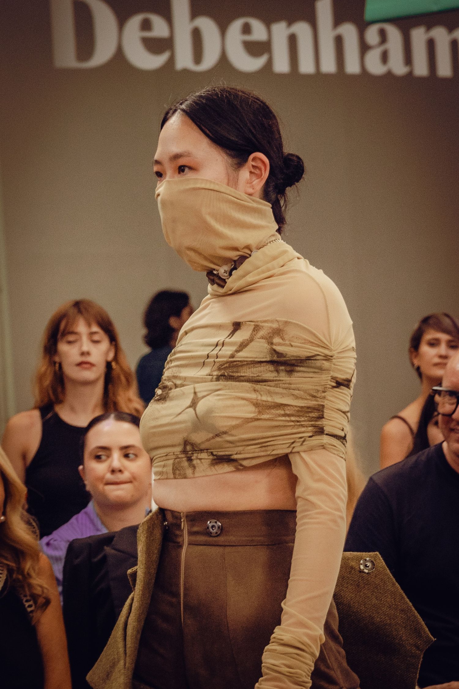 Runway model wearing tan draped ensemble with face covering at Debenhams fashion show.