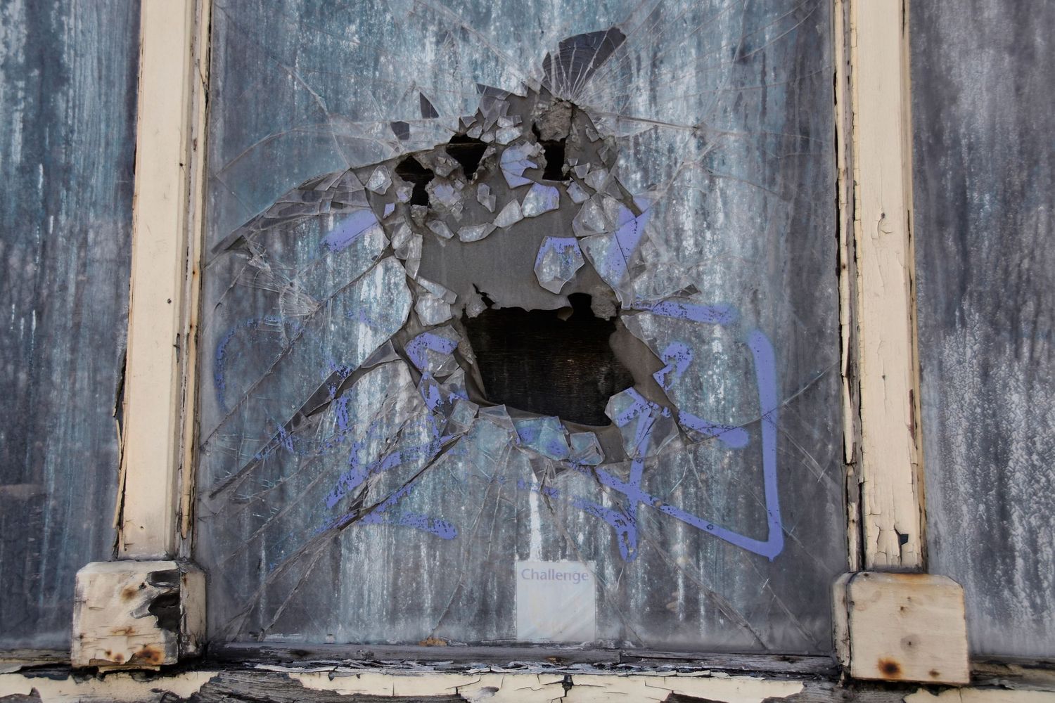 Close-up of broken window with splintered glass and hole in weathered frame.