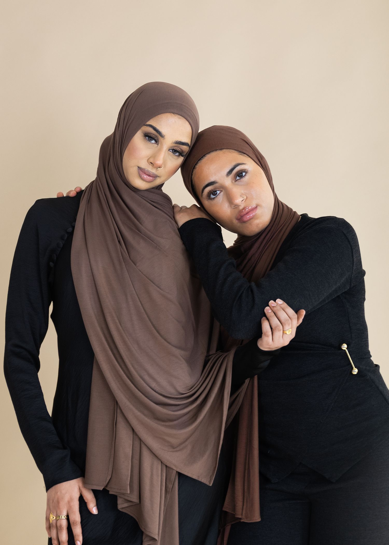 Two people in black and brown hijabs pose together in a series of casual portrait shots against a light background.