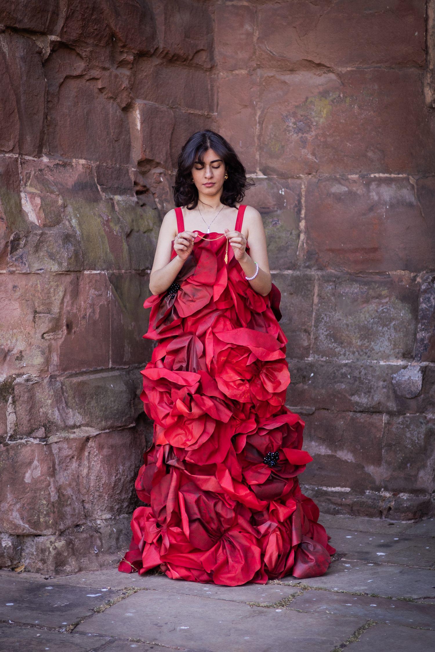 A dramatic red ruffled dress photographed in sequence against a weathered stone wall background.