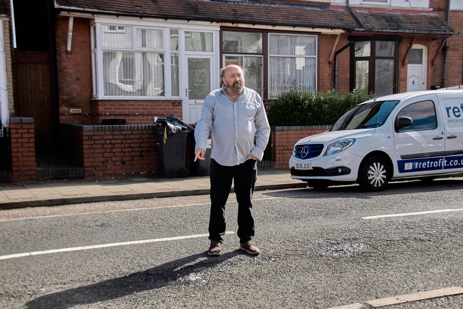 Person standing on a residential street next to a parked car on a cloudy day.
