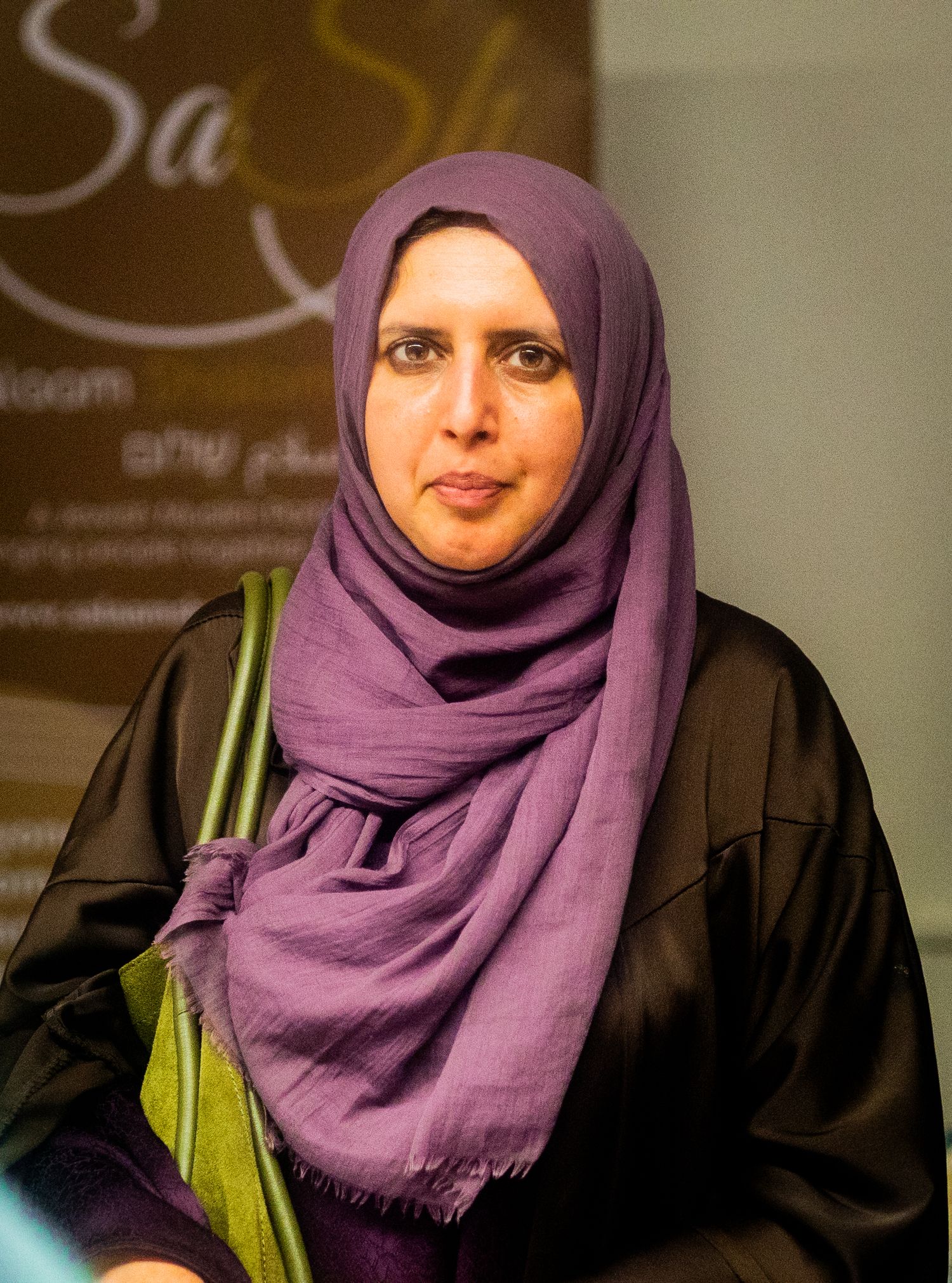 Indoor portrait with purple hijab and black garment against business signage.