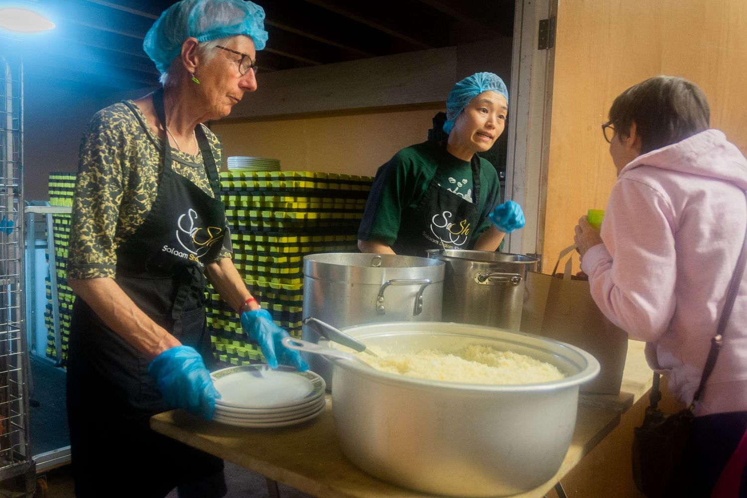 Food service workers prepare large batches of food in industrial-sized mixing bowls.