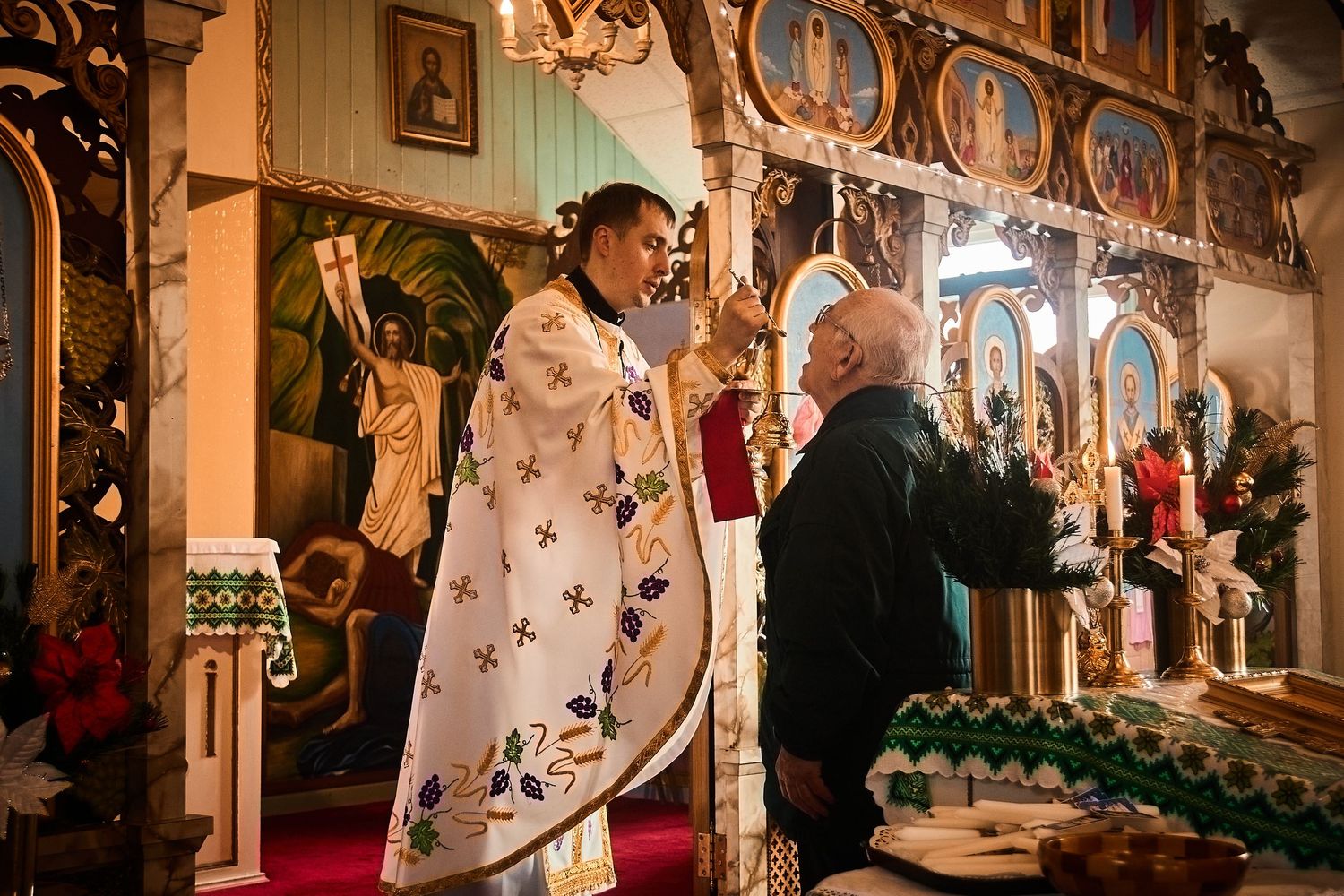 Warm-lit church interior showing traditional Orthodox iconography and Christmas decorations.