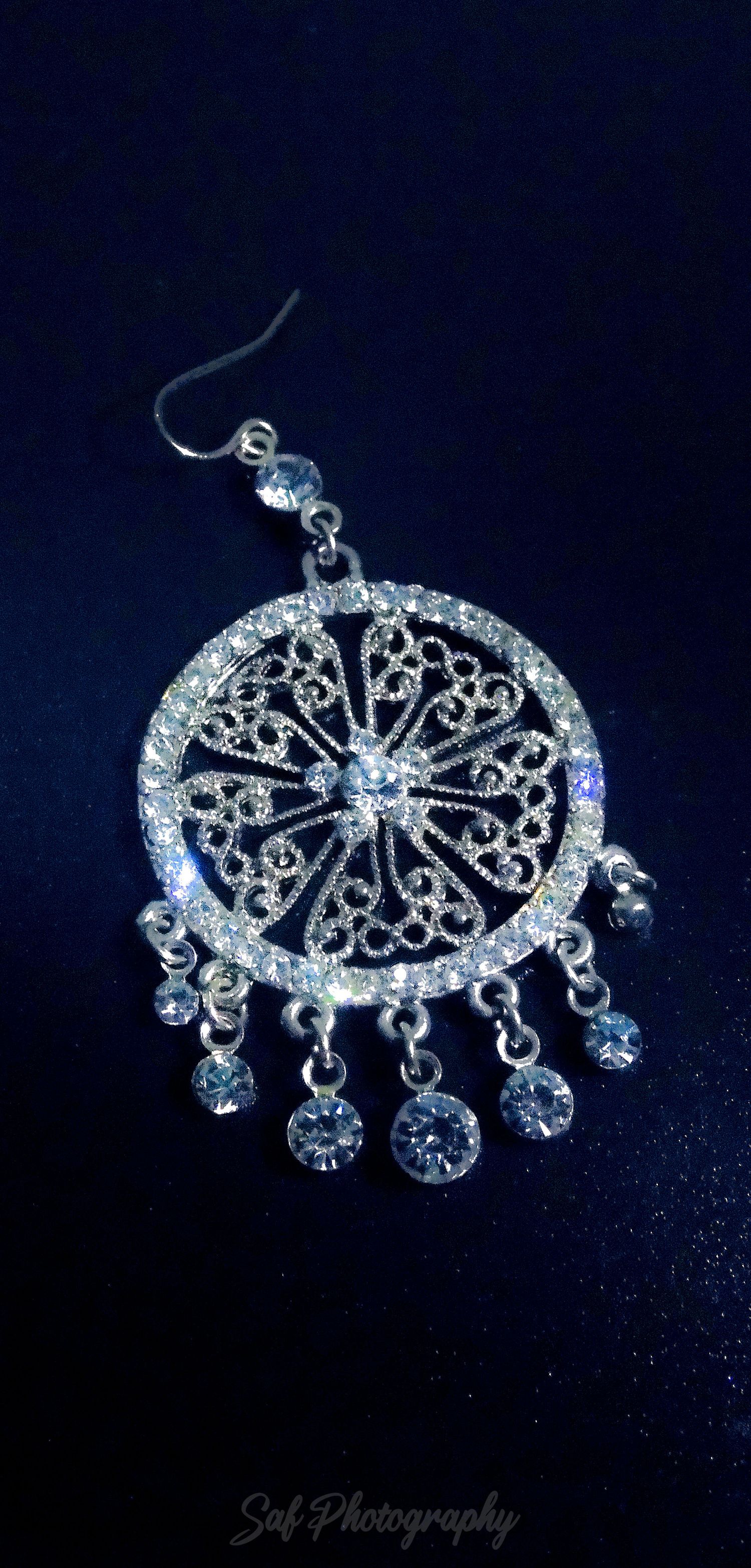Elegant silver chandelier-style earring with crystal accents and dangling jewels on a dark background.